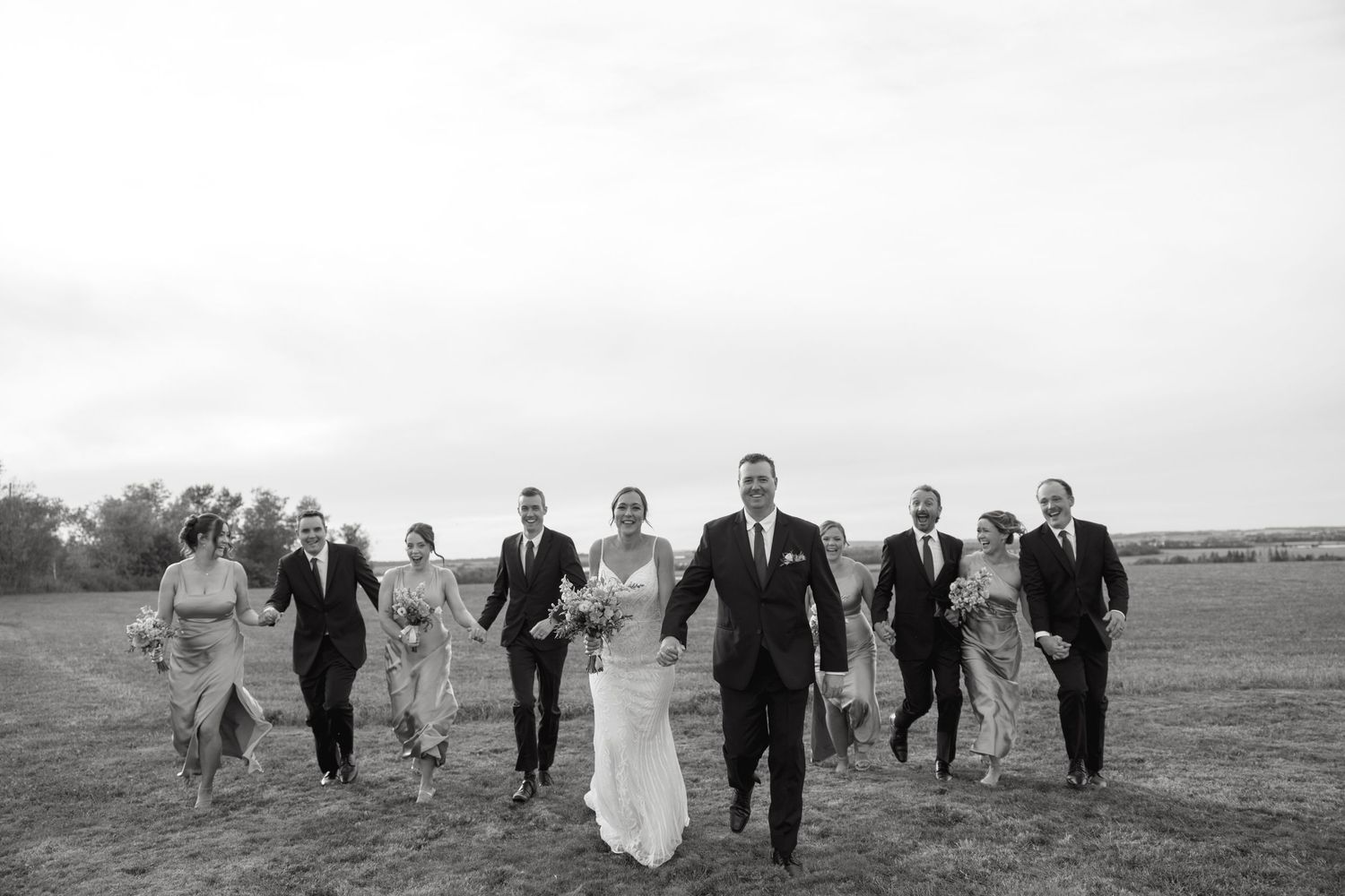 Wedding party walks together across a scenic open field landscape.