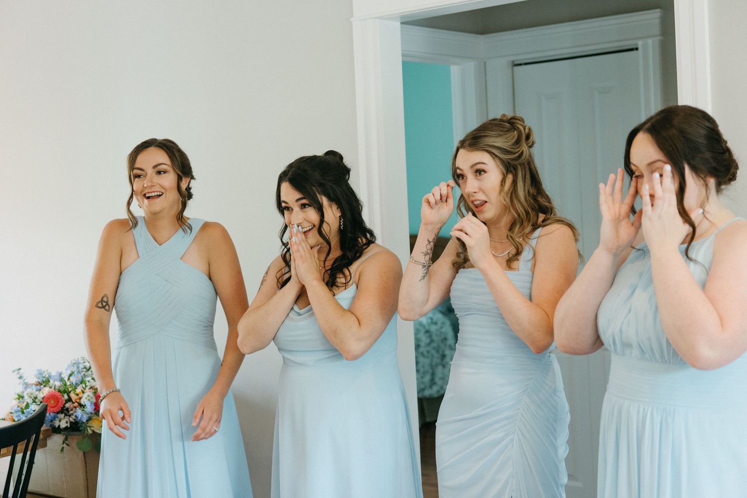 Bridesmaids in light blue dresses share emotional reactions during a wedding moment.