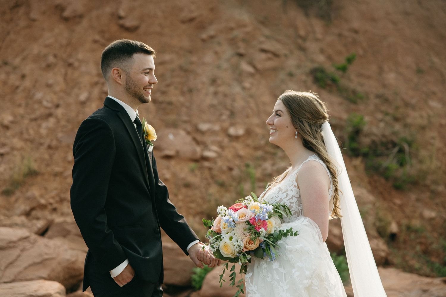 Wedding couple walking along rocky beach landscape during photo session.