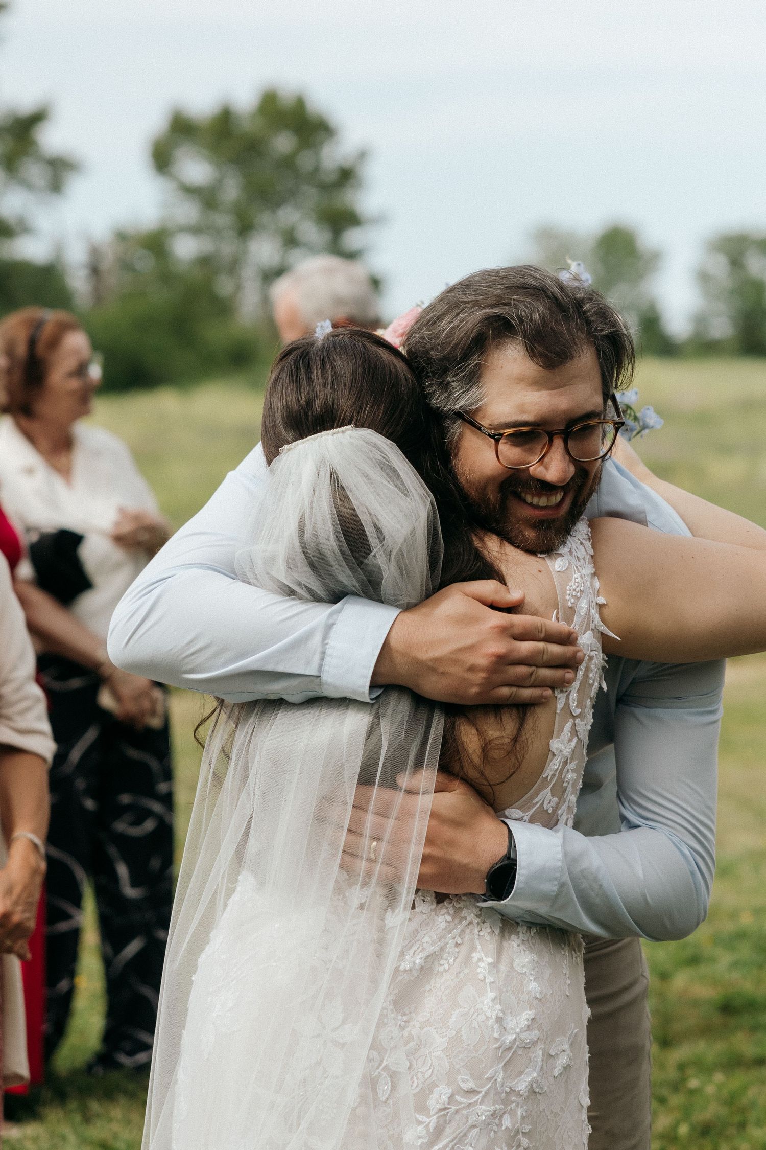 A joyful embrace is shared between wedding attendees during an outdoor celebration.