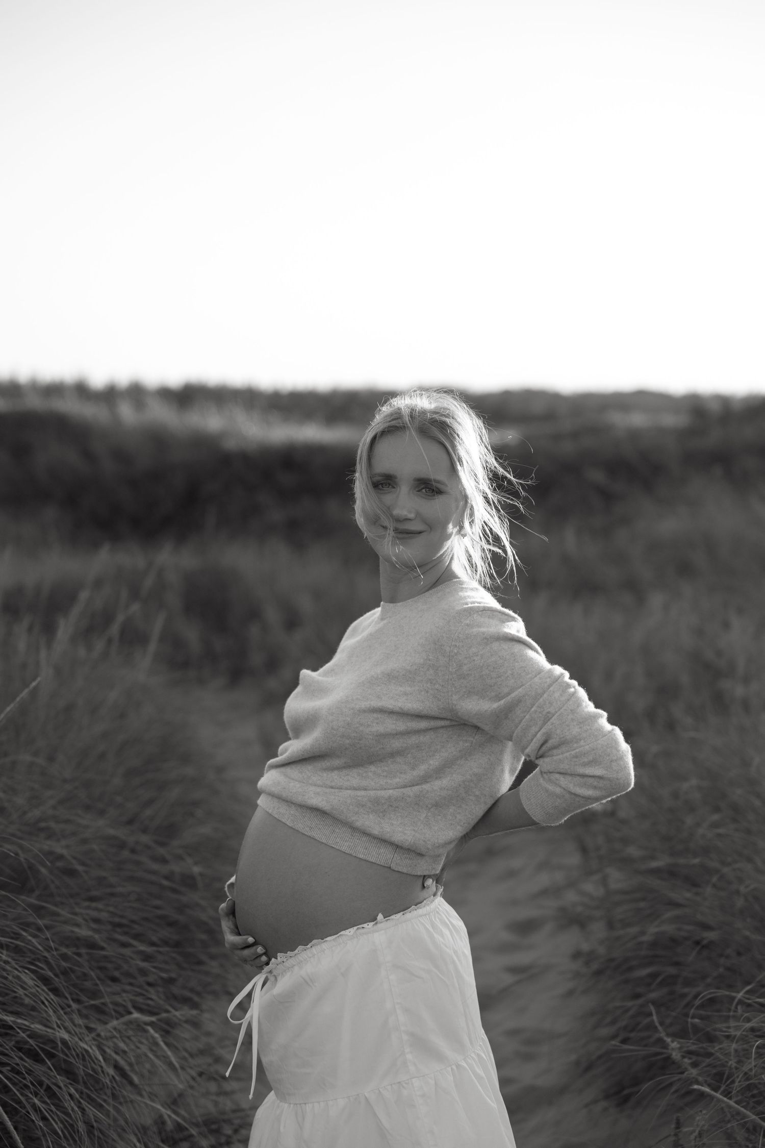 Black and white maternity portrait showing pregnant belly against natural landscape.