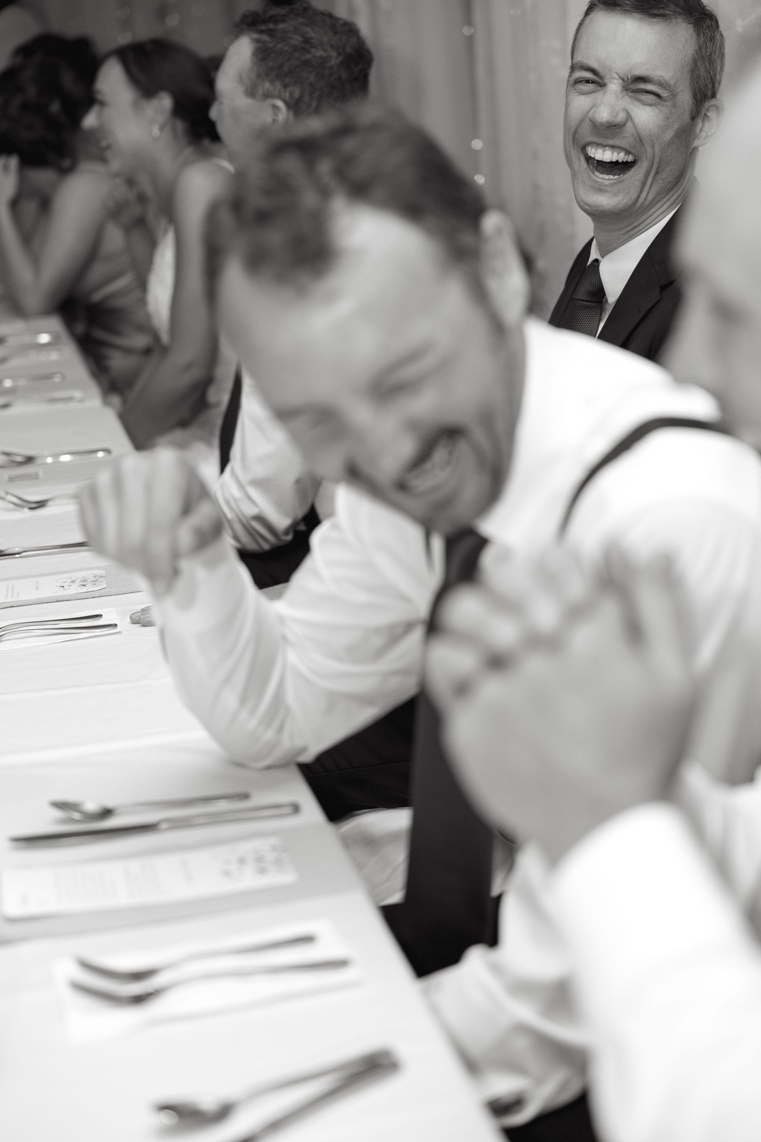 Guests laughing and enjoying themselves at a formal dining event with white tablecloths.