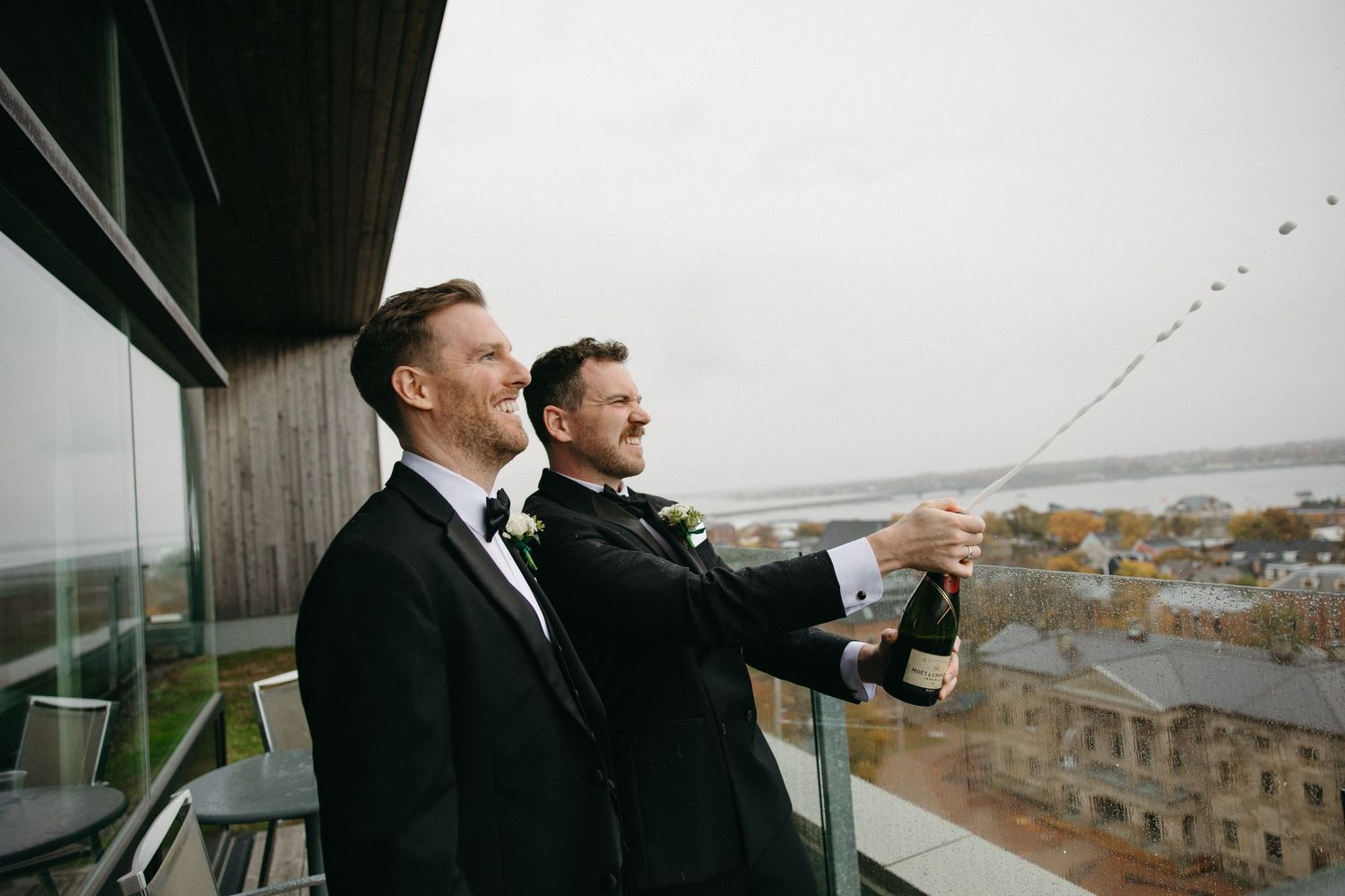 Two people in formal wear look out over a cityscape from a balcony or rooftop.