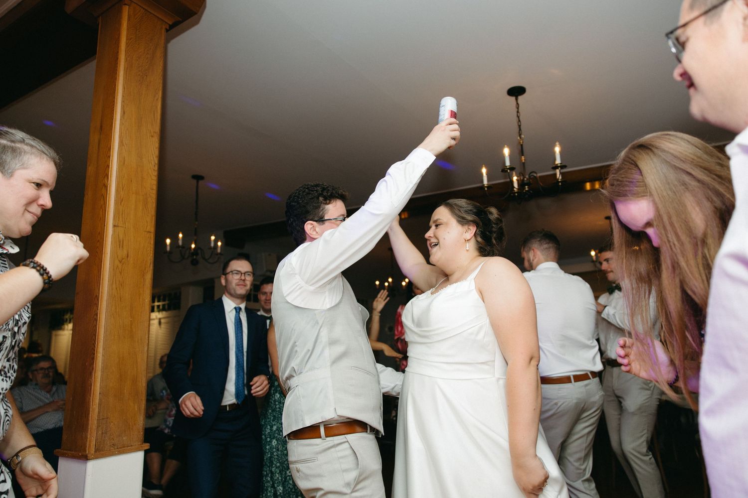 Bride and groom dancing joyfully with guests at indoor wedding reception celebration.