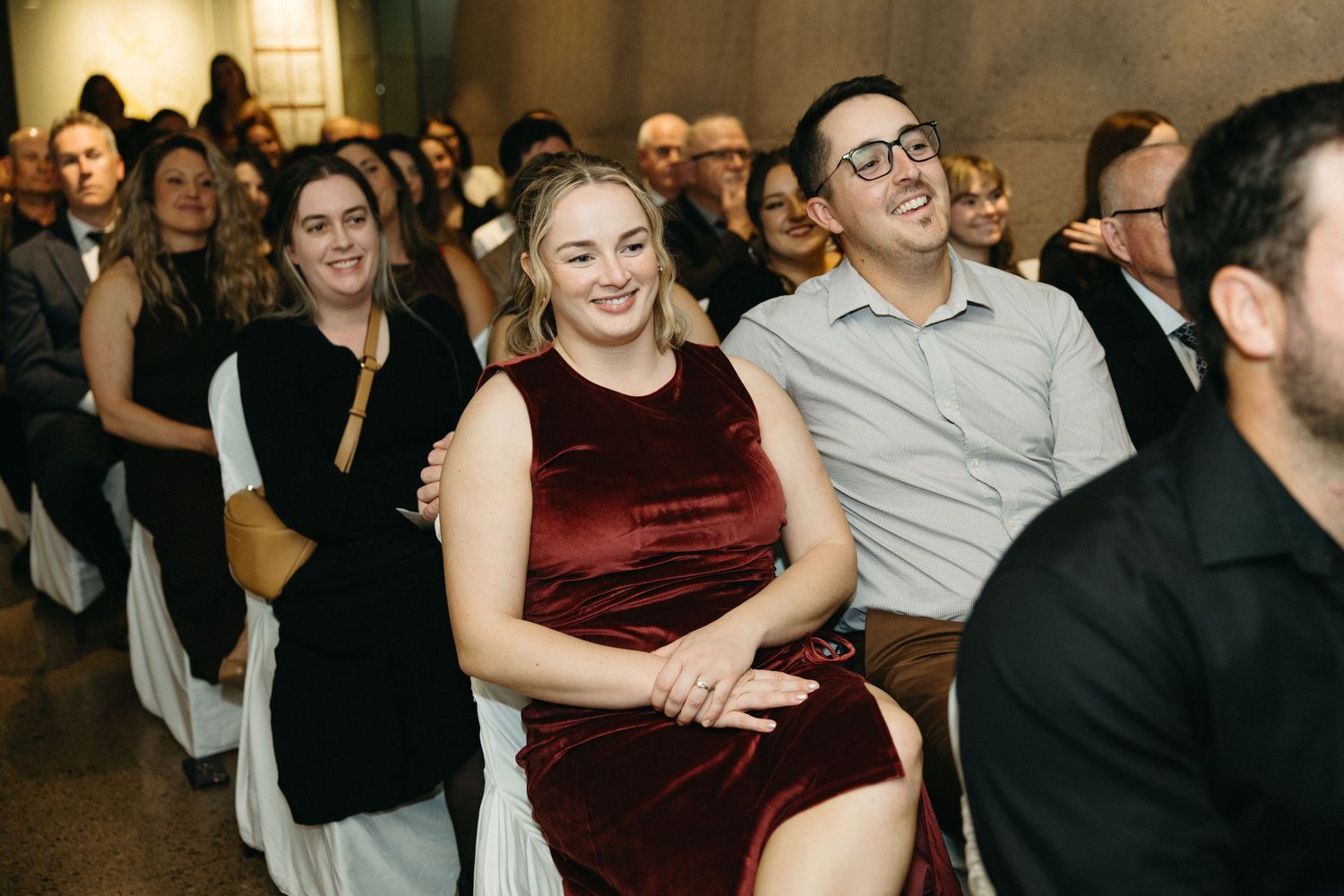 Audience members seated in rows showing engaged expressions during an indoor event.