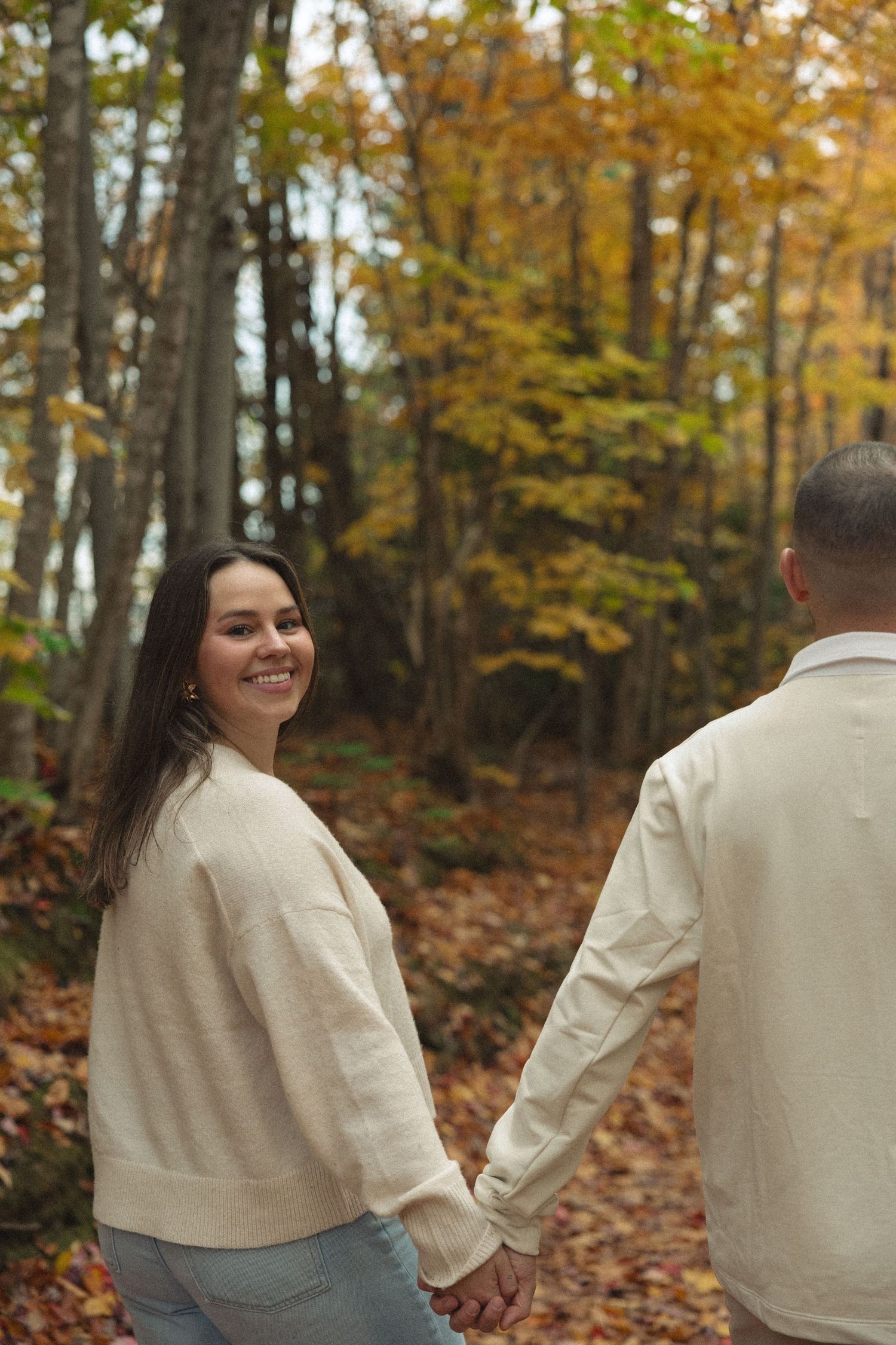 Two people share a playful moment walking together on a trail covered in fall foliage.