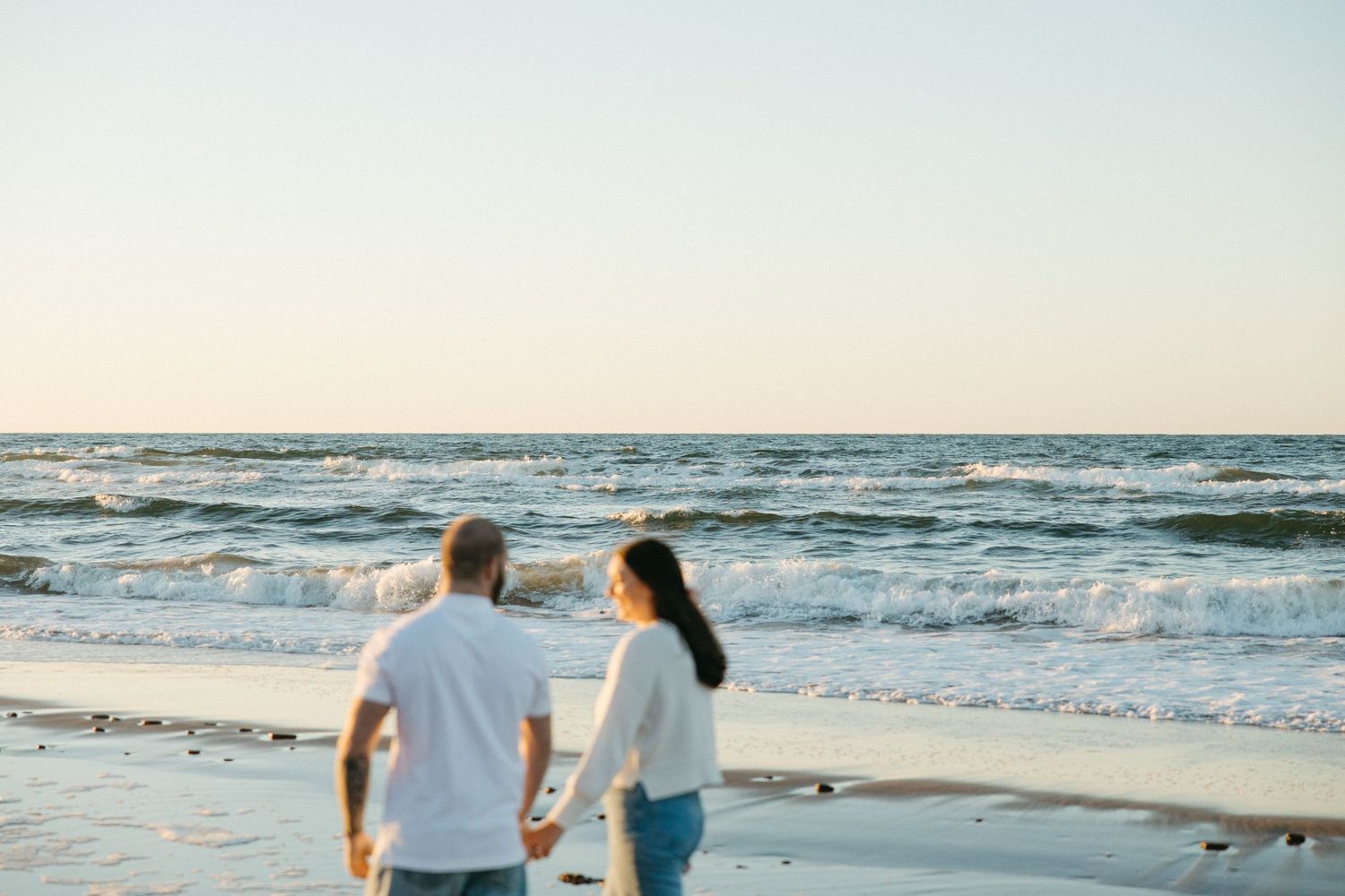 Couple strolling along peaceful beach shoreline at dusk.