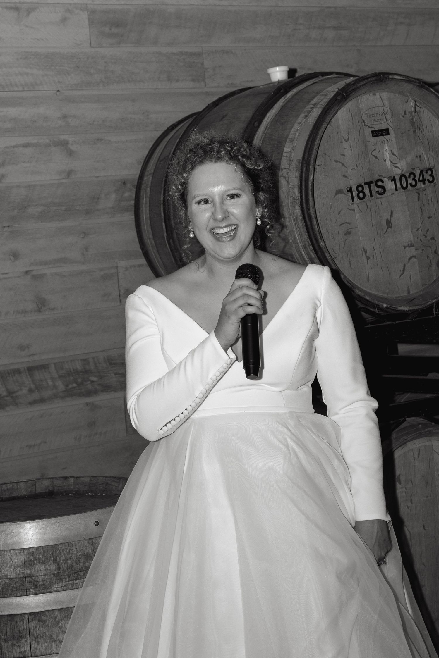 Wedding guests in formal attire posing near wooden wine barrels.