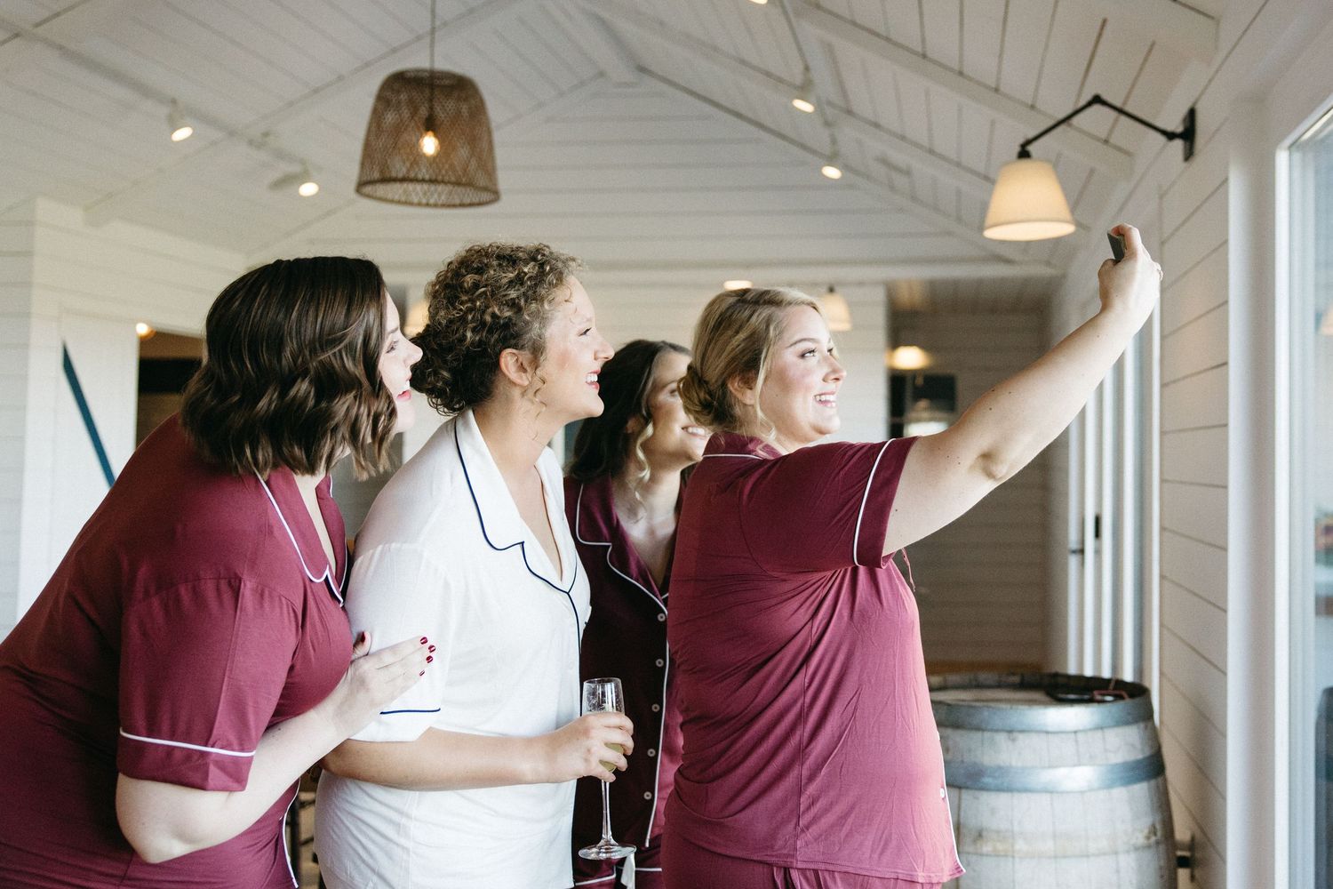 Friends in burgundy outfits embrace and laugh together in a bright room with white walls.