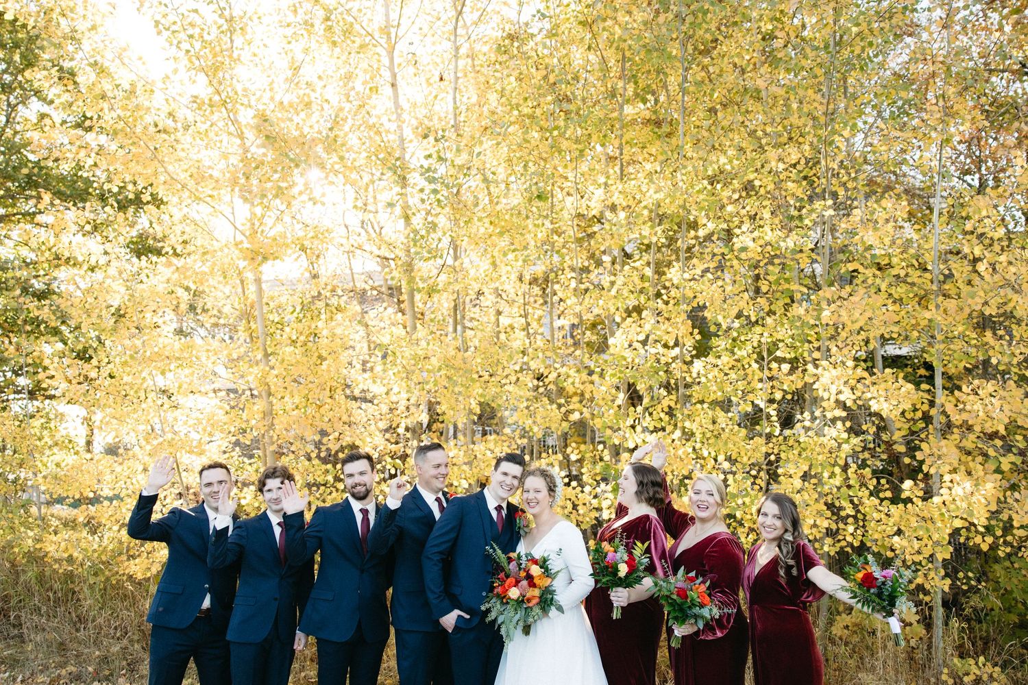 Joyful wedding party celebration photo against golden fall foliage background.