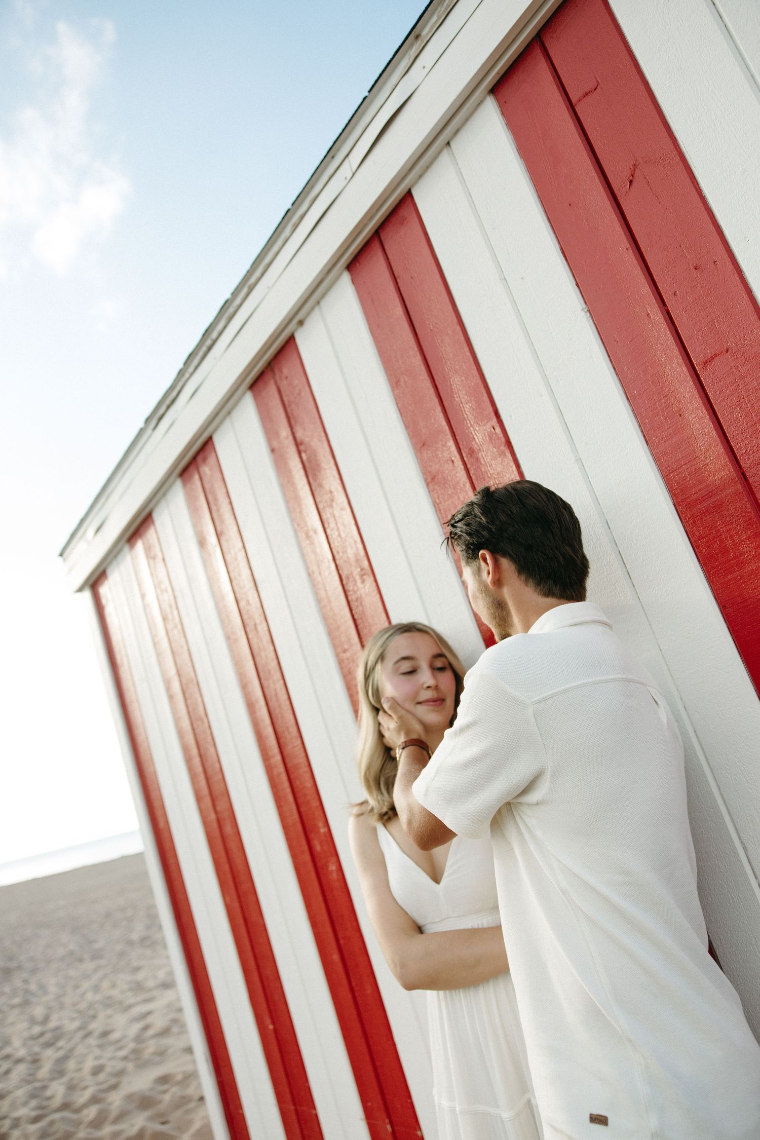 Couple embracing by red and white striped beach hut.