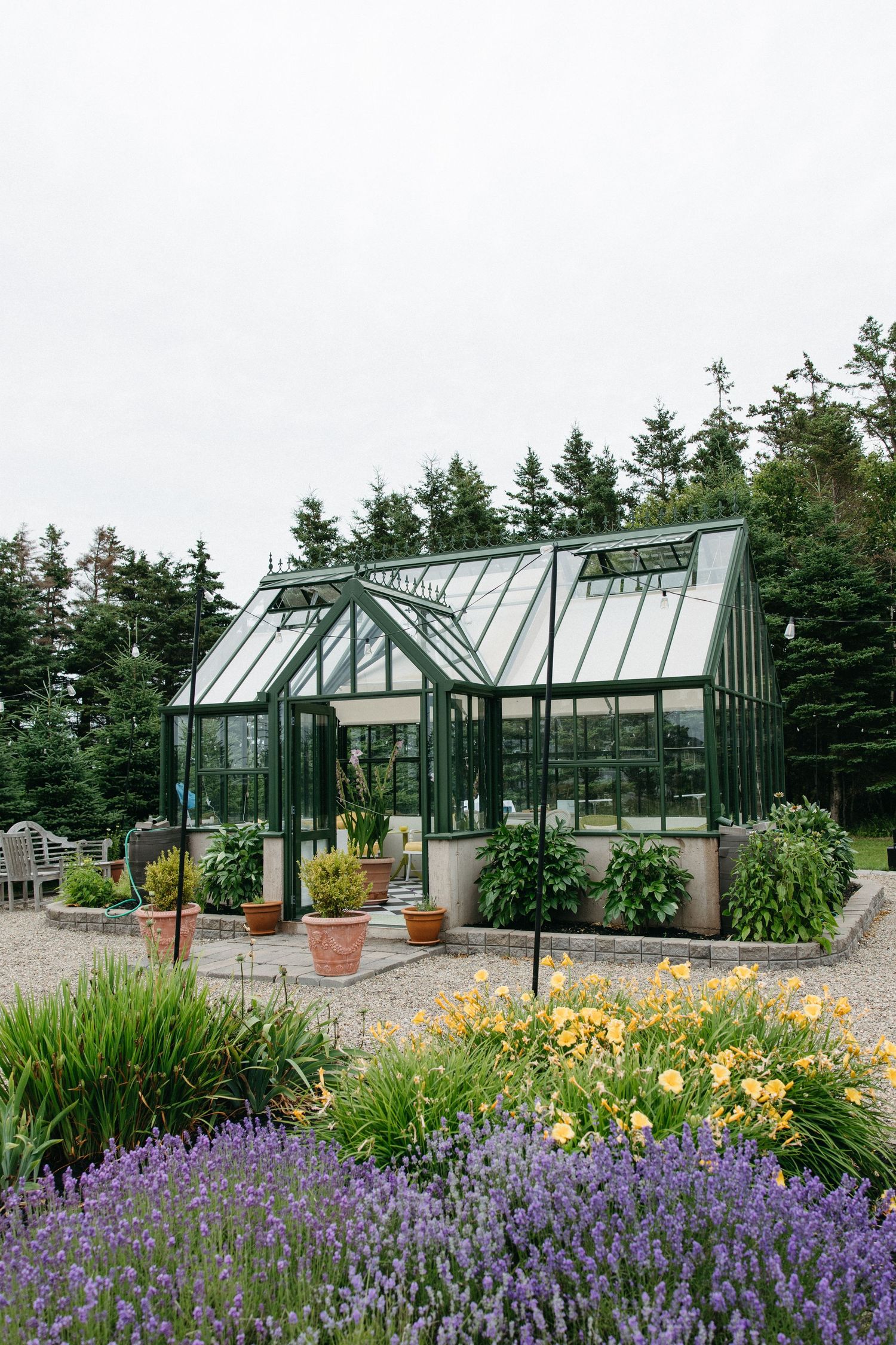 Elegant glass greenhouse surrounded by lavender and yellow flowers in lush garden setting.