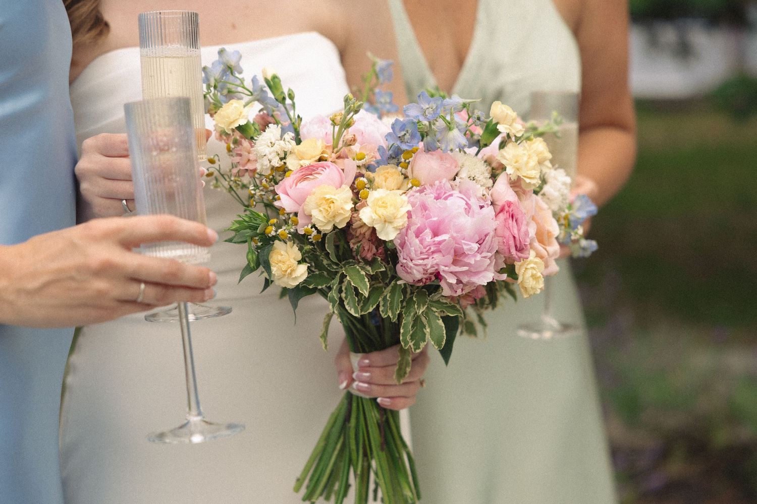 Bride holding colorful pink and yellow wedding bouquet with champagne flutes nearby.