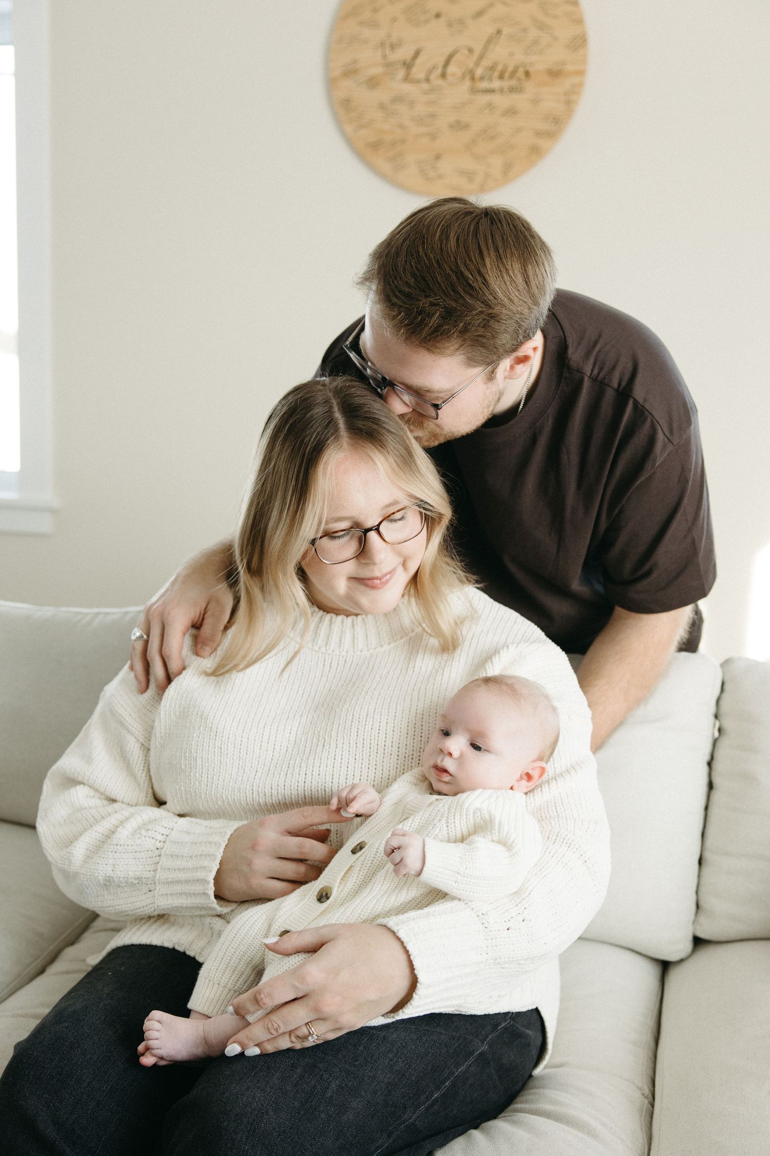 A tender family moment on a white couch as they cuddle with their baby in a cream sweater.