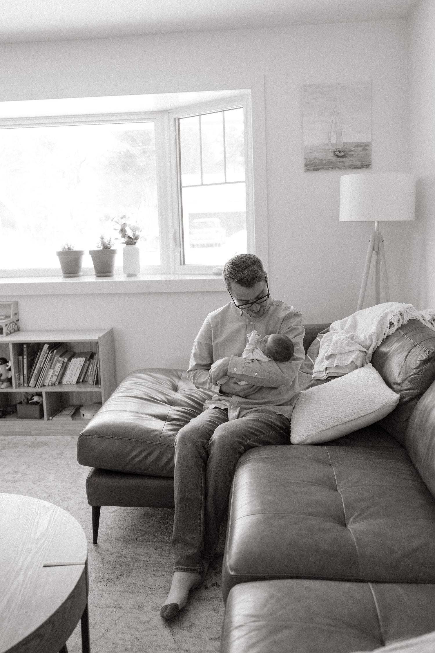 Black and white photos of relaxed moments on a leather couch with parent and infant.