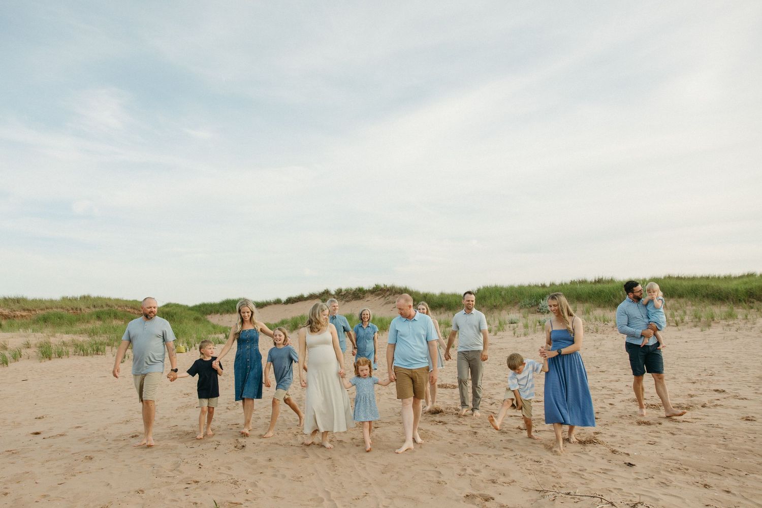 An extended family in blue and white outfits walks together across a wide sandy beach.