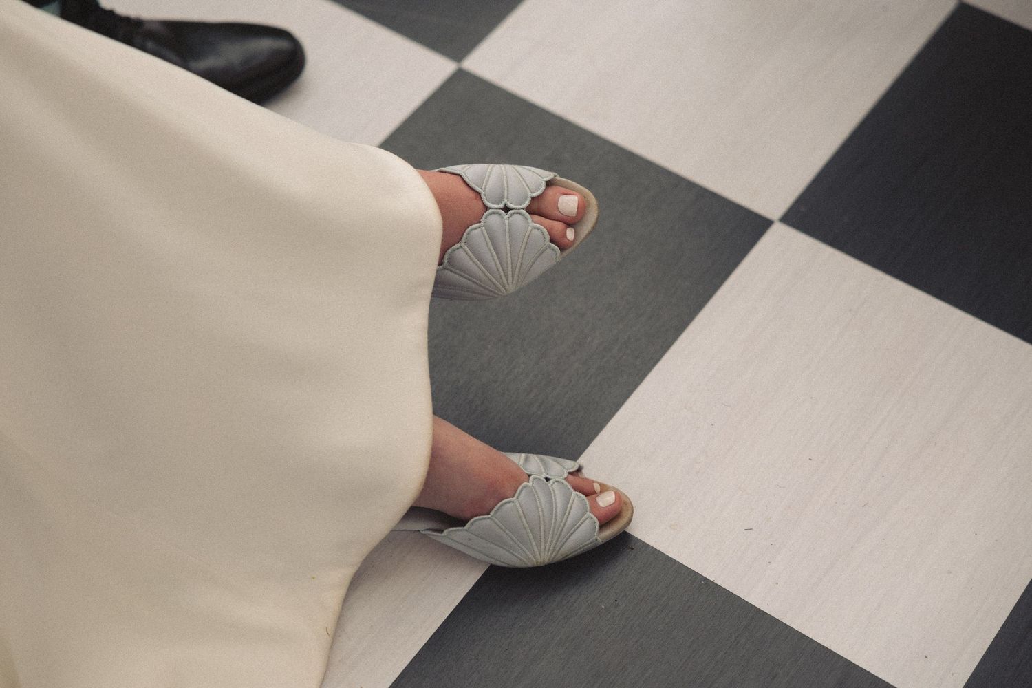 Close-up of brides feet in light gray open-toe heels on black and white checkered floor.