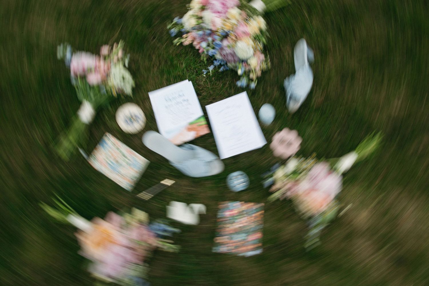 A swirling aerial shot captures wedding stationery, flowers, and decorative items arranged on green grass.