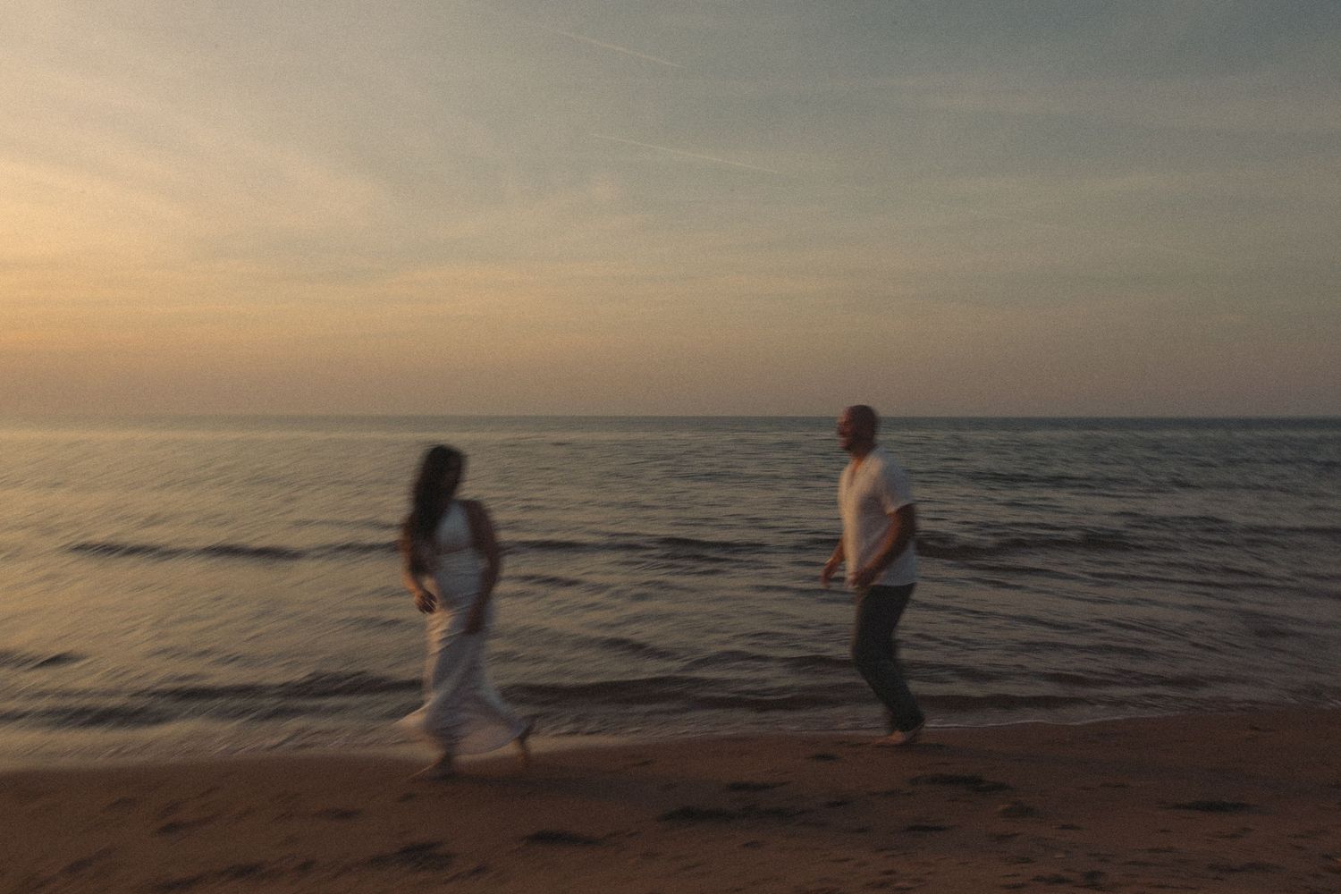 A couple walks hand in hand along a sandy beach during a beautiful golden sunset.