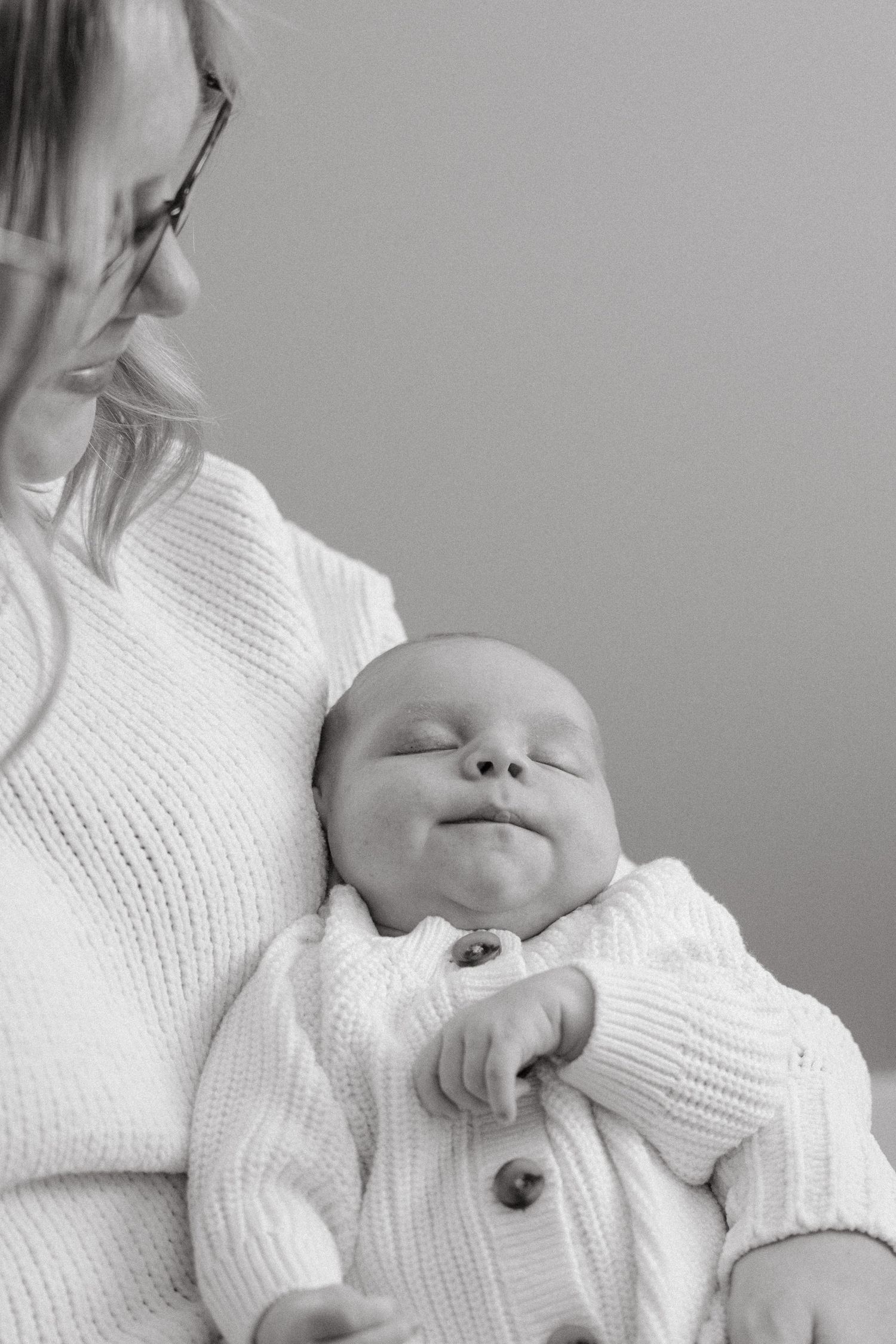 Person in white sweater holding sleeping baby against their chest.