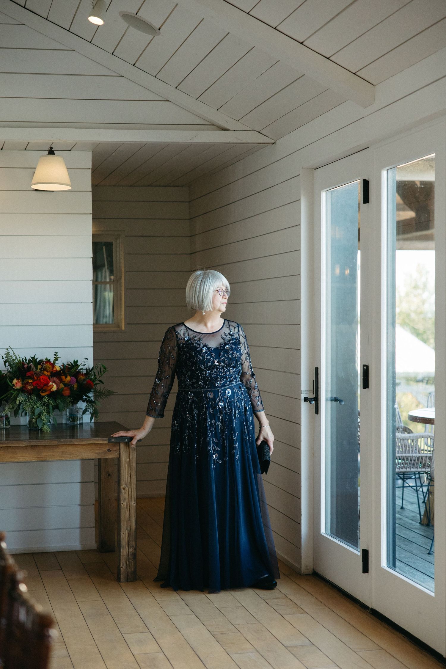 Woman in elegant navy blue sequined gown standing in bright white modern farmhouse interior.