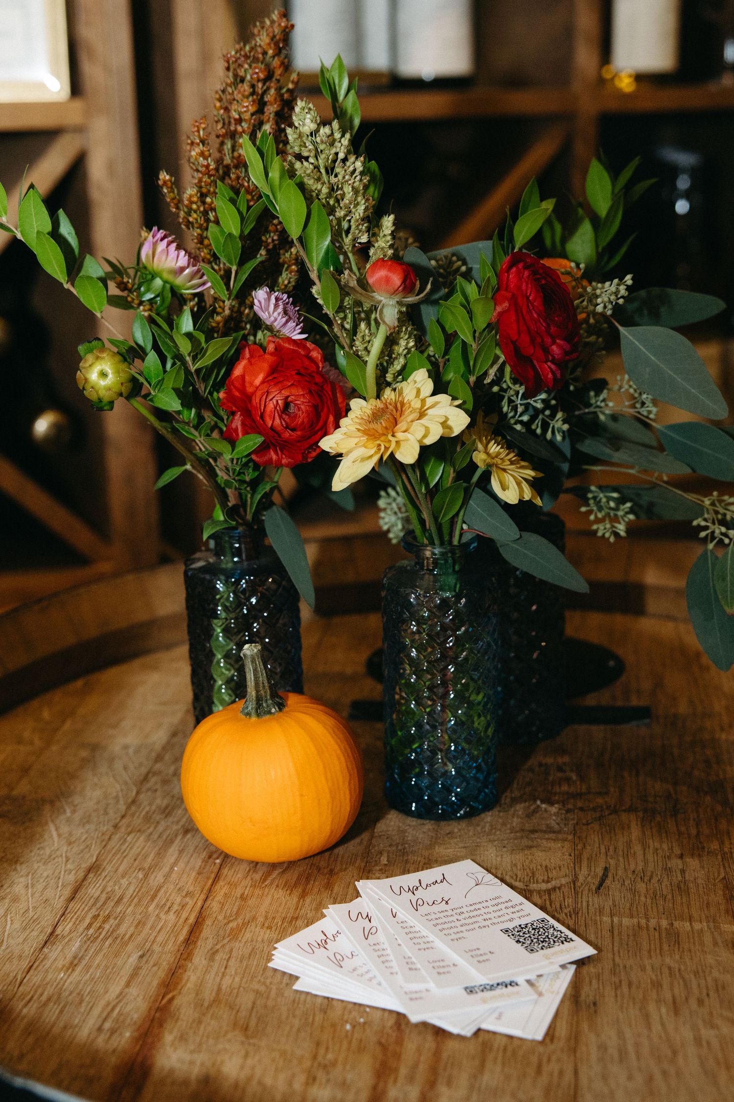 Colorful floral arrangements in pumpkin vases with event tickets displayed on a rustic wooden table.