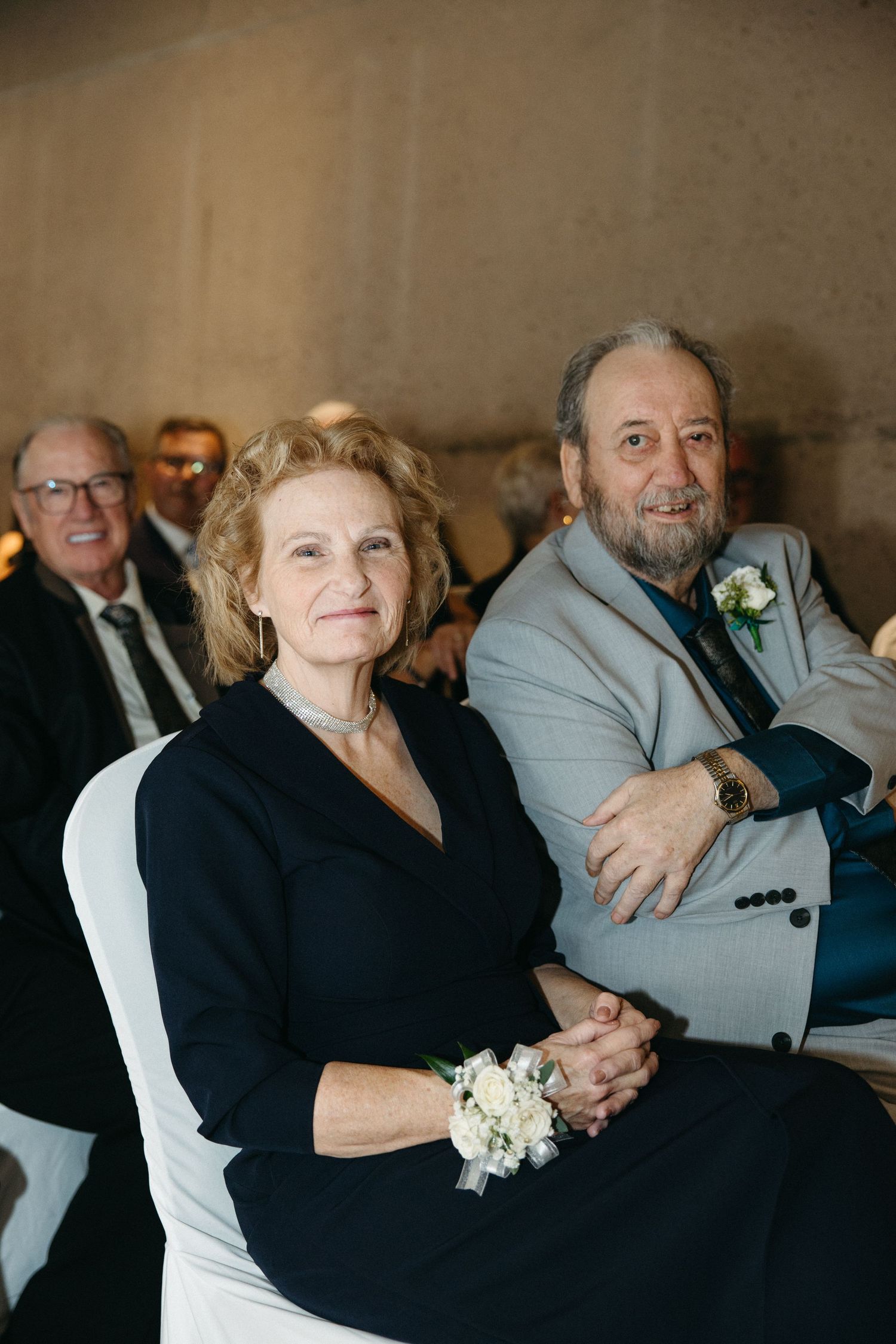 Elderly wedding guests in formal attire sharing an intimate moment during the celebration.