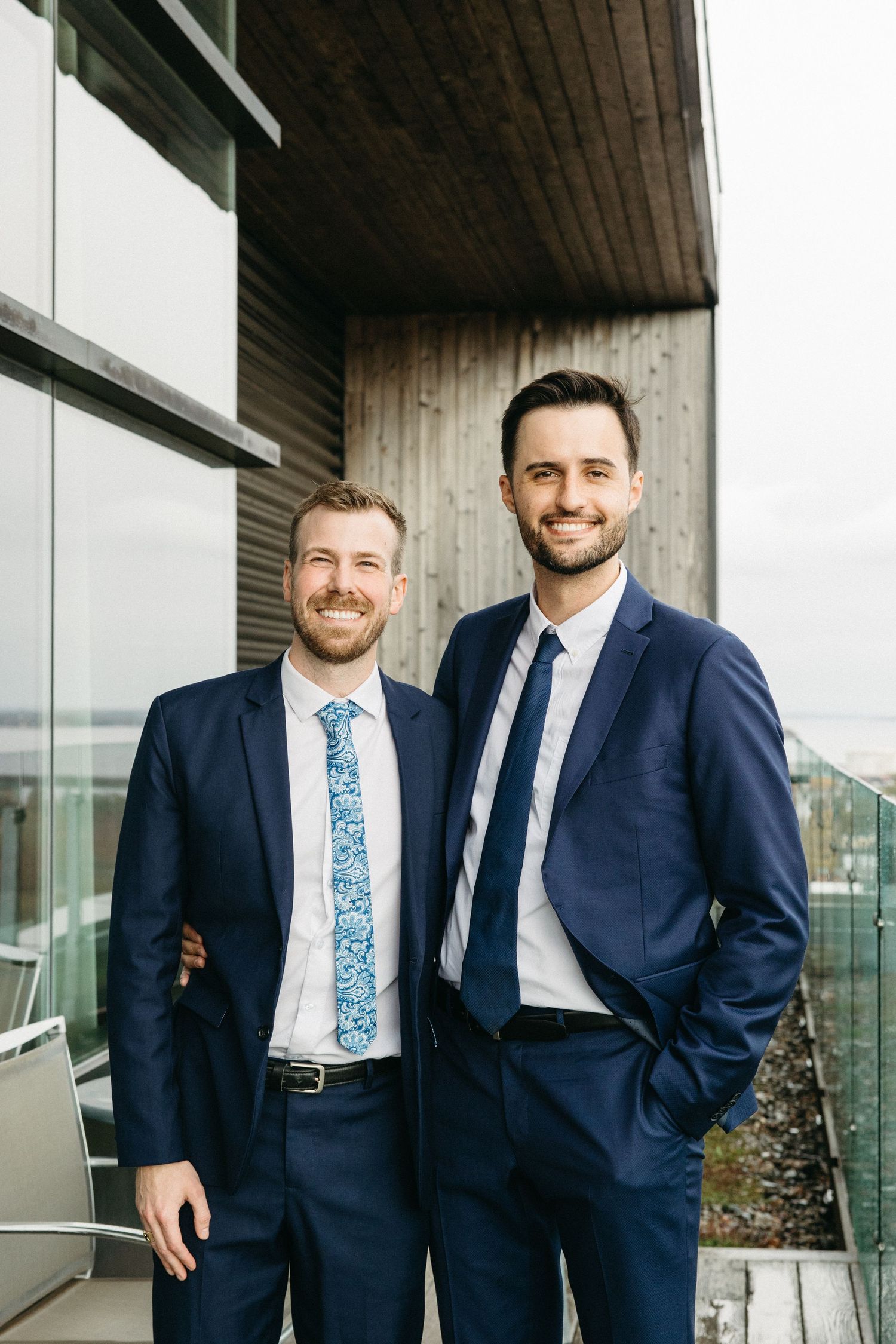 Three men in navy suits and floral ties smile together during a formal event.