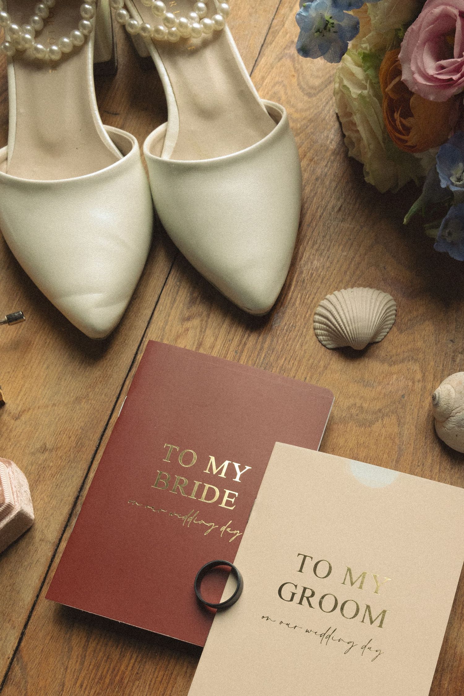Wedding accessories including white shoes, cards, and floral details arranged on wooden flooring.