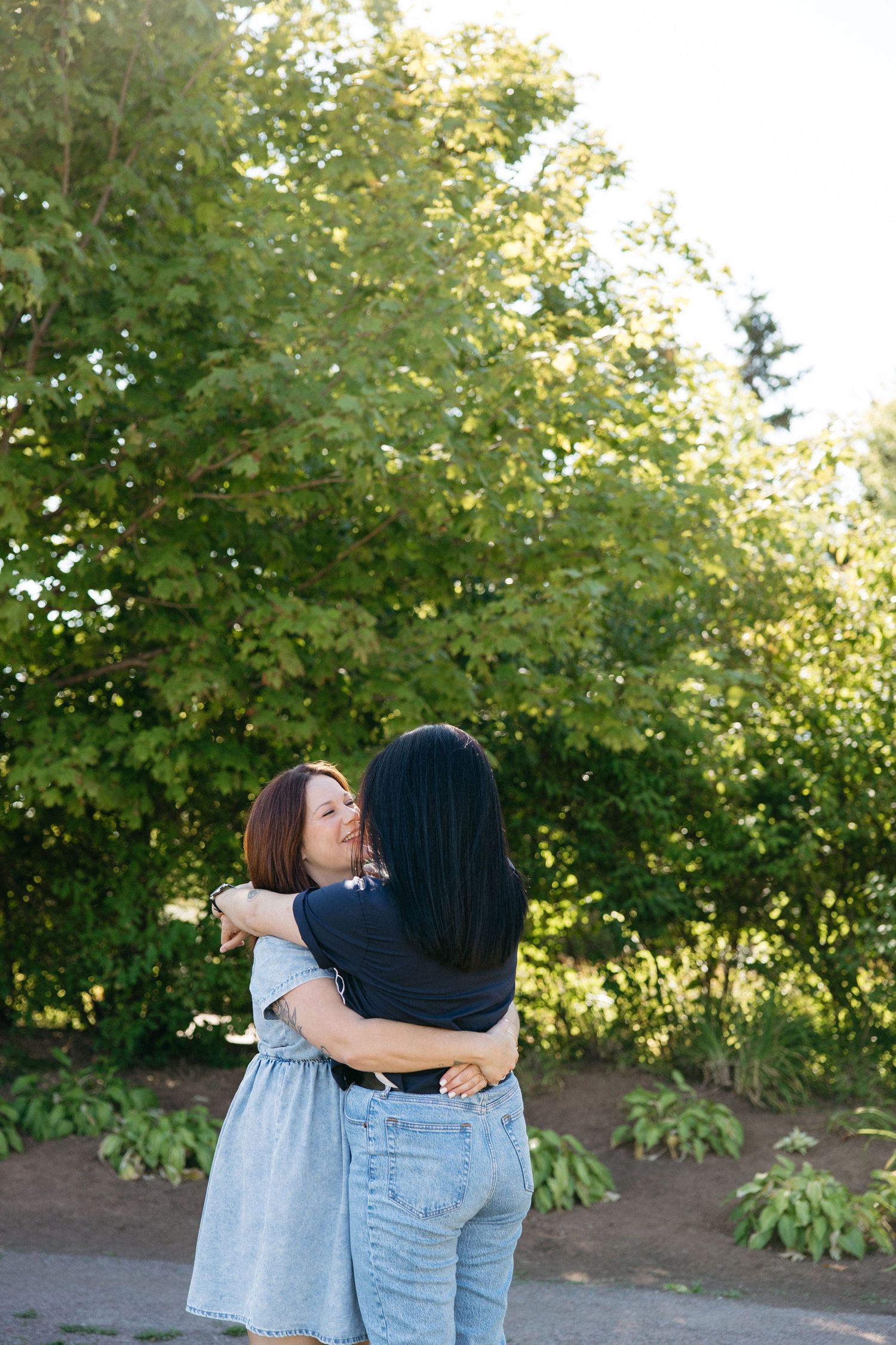Two people sharing a warm hug outdoors with sunlit trees in the background.