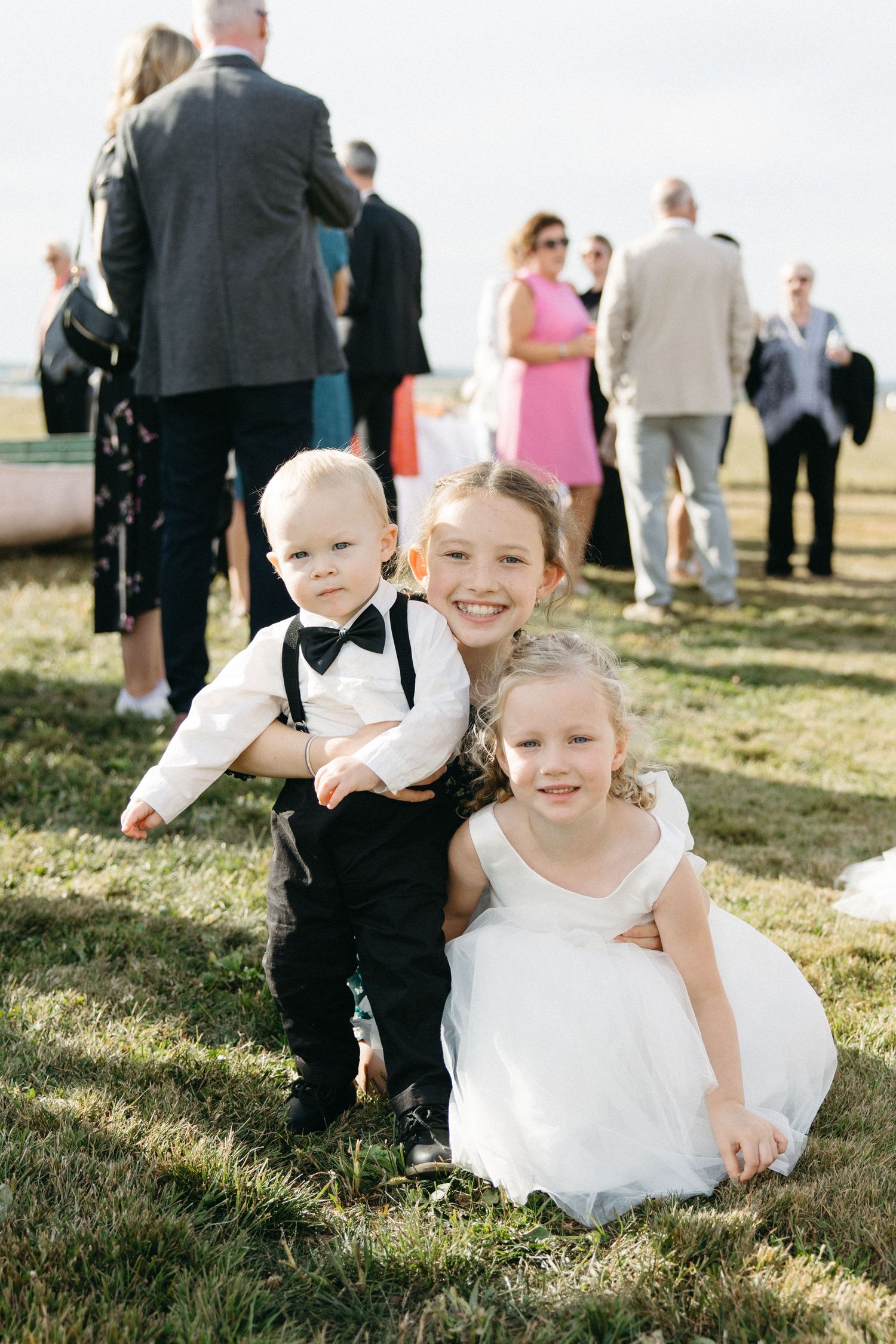 Young attendants in formal wear playing on the grass during a wedding celebration.
