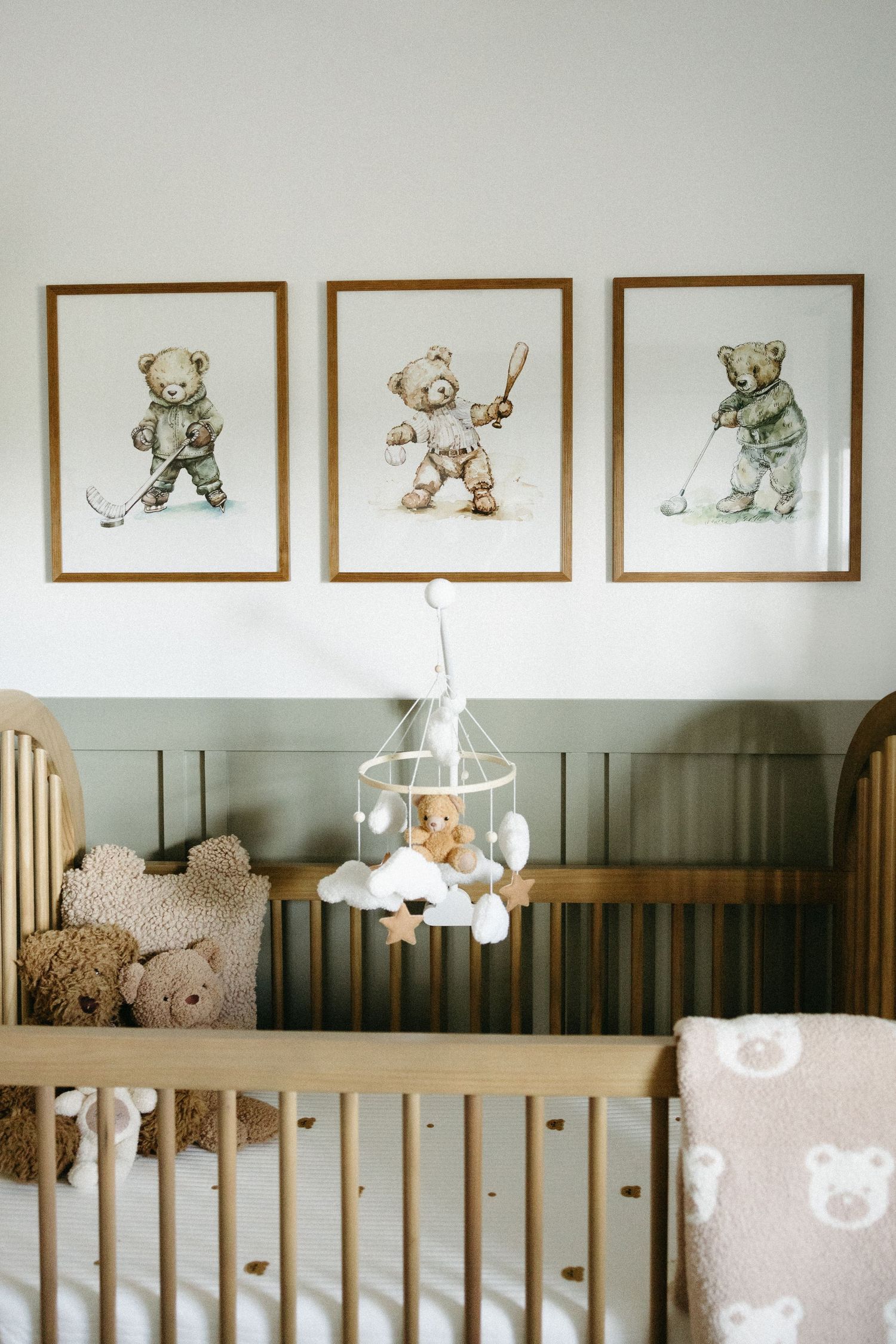 A nursery room with framed animal artwork above a wooden crib and decorative wall paneling.