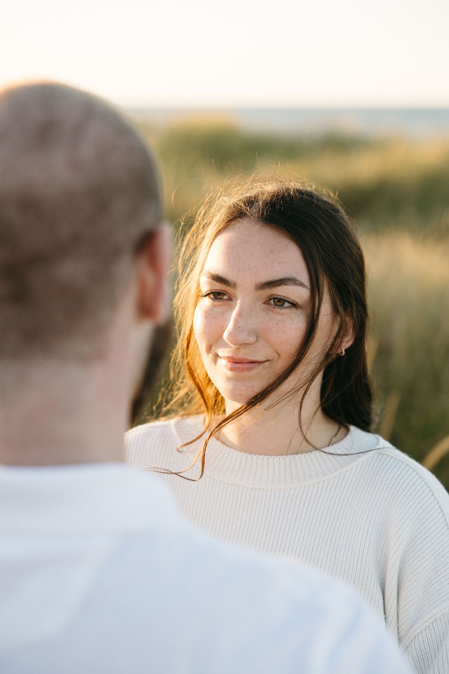 Person in white sweater smiles warmly during sunset photoshoot outdoors.