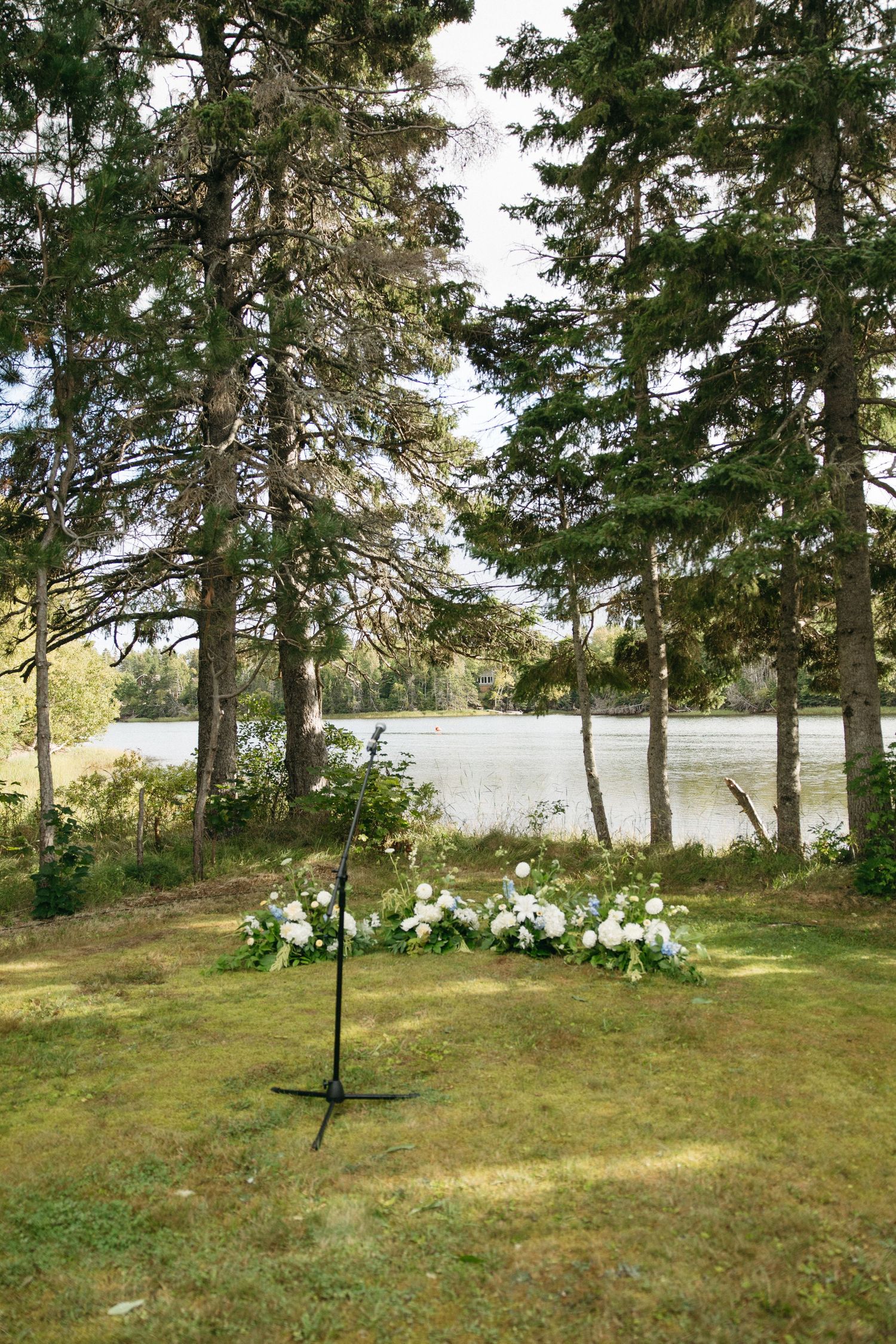 Peaceful lakeside setting with pine trees and floral arrangements on a grassy slope.