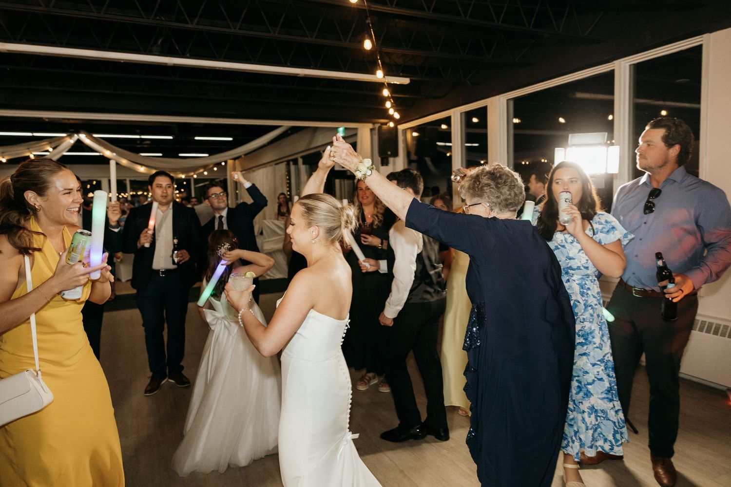 Guests celebrate on the dance floor at a wedding reception with string lights overhead.