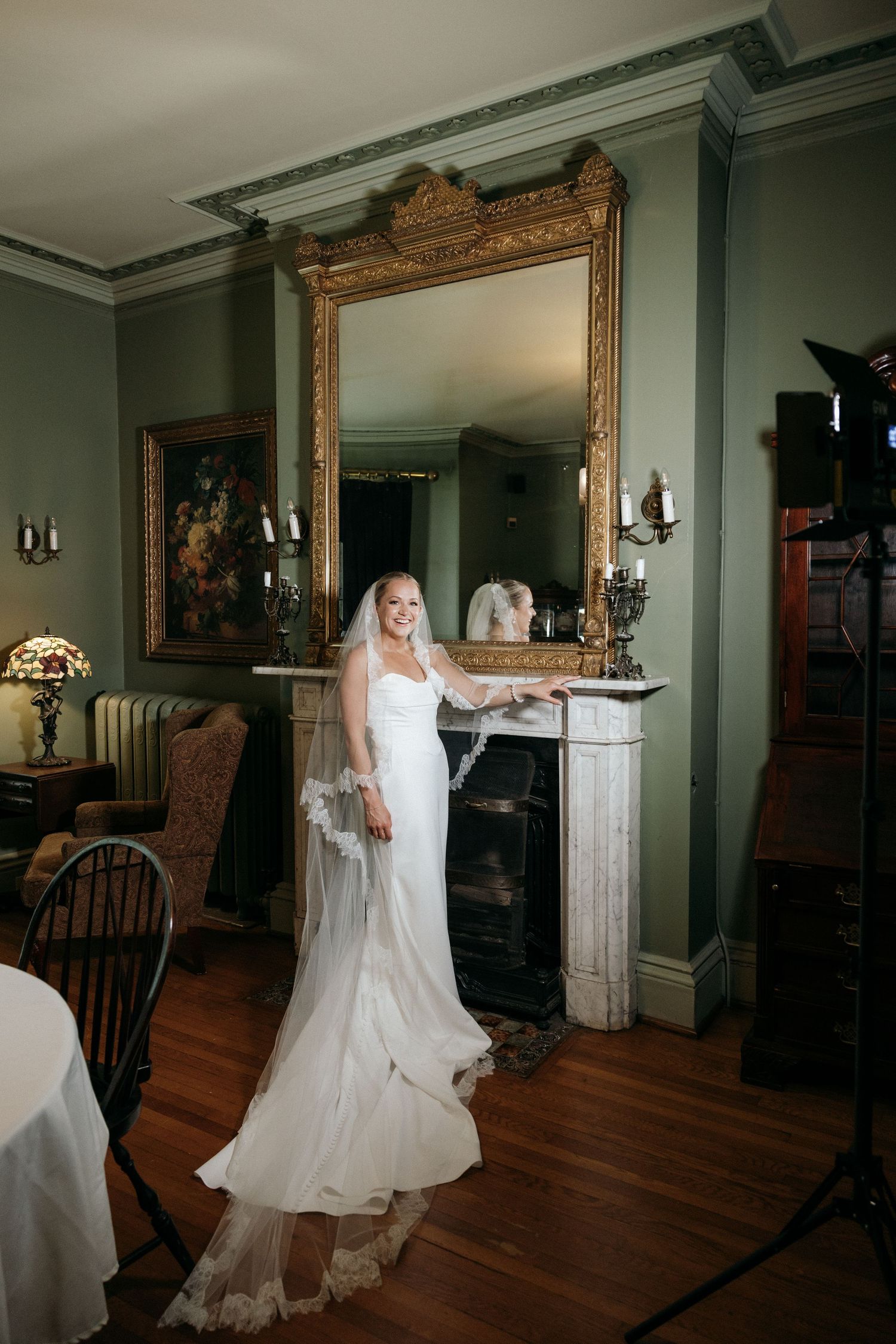 A bride in a flowing white dress twirls in an elegant room with hardwood floors and ornate mirrors.