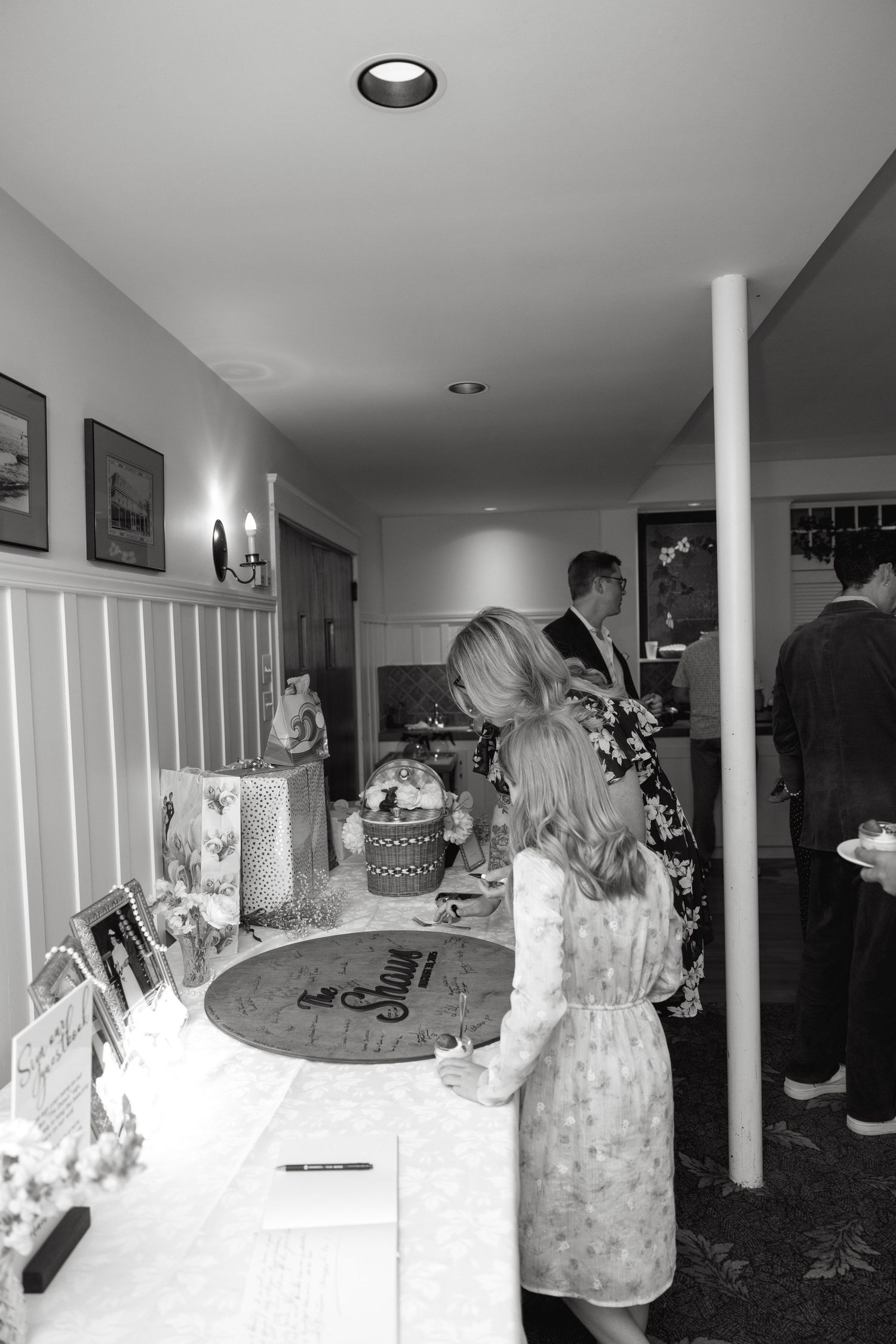 Guests signing a wedding guestbook at a decorated table during a wedding reception in black and white.