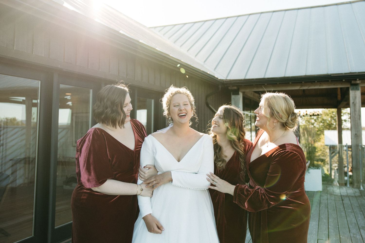 Sun-lit wedding scene on a wooden deck with flowing white dress and dark attire.