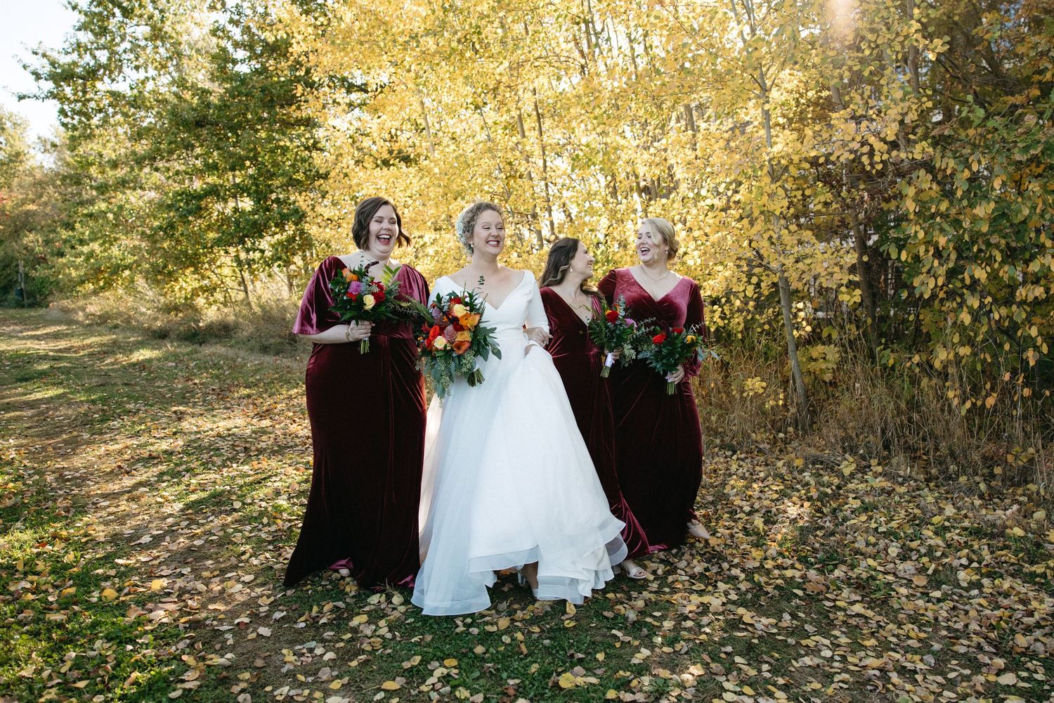 Wedding party laughing together surrounded by golden autumn leaves.