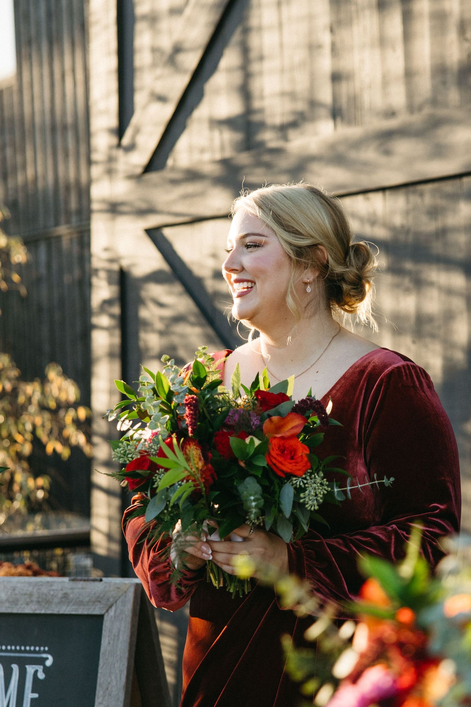 Bridesmaids in burgundy velvet dresses hold vibrant red and green floral bouquets.