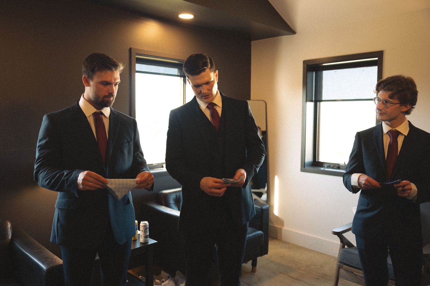 Men in suits gather near windows during wedding day preparations.