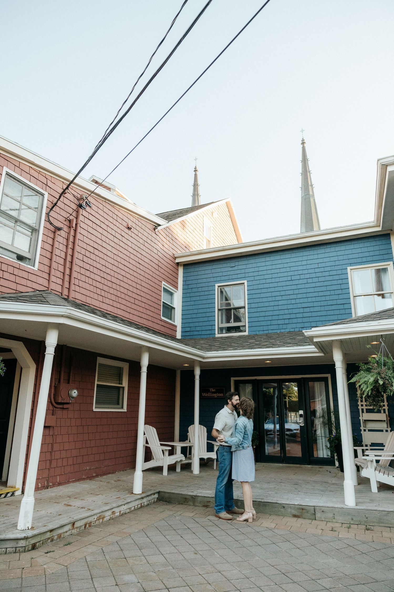 Two people converse under a covered porch area of a blue and red building.