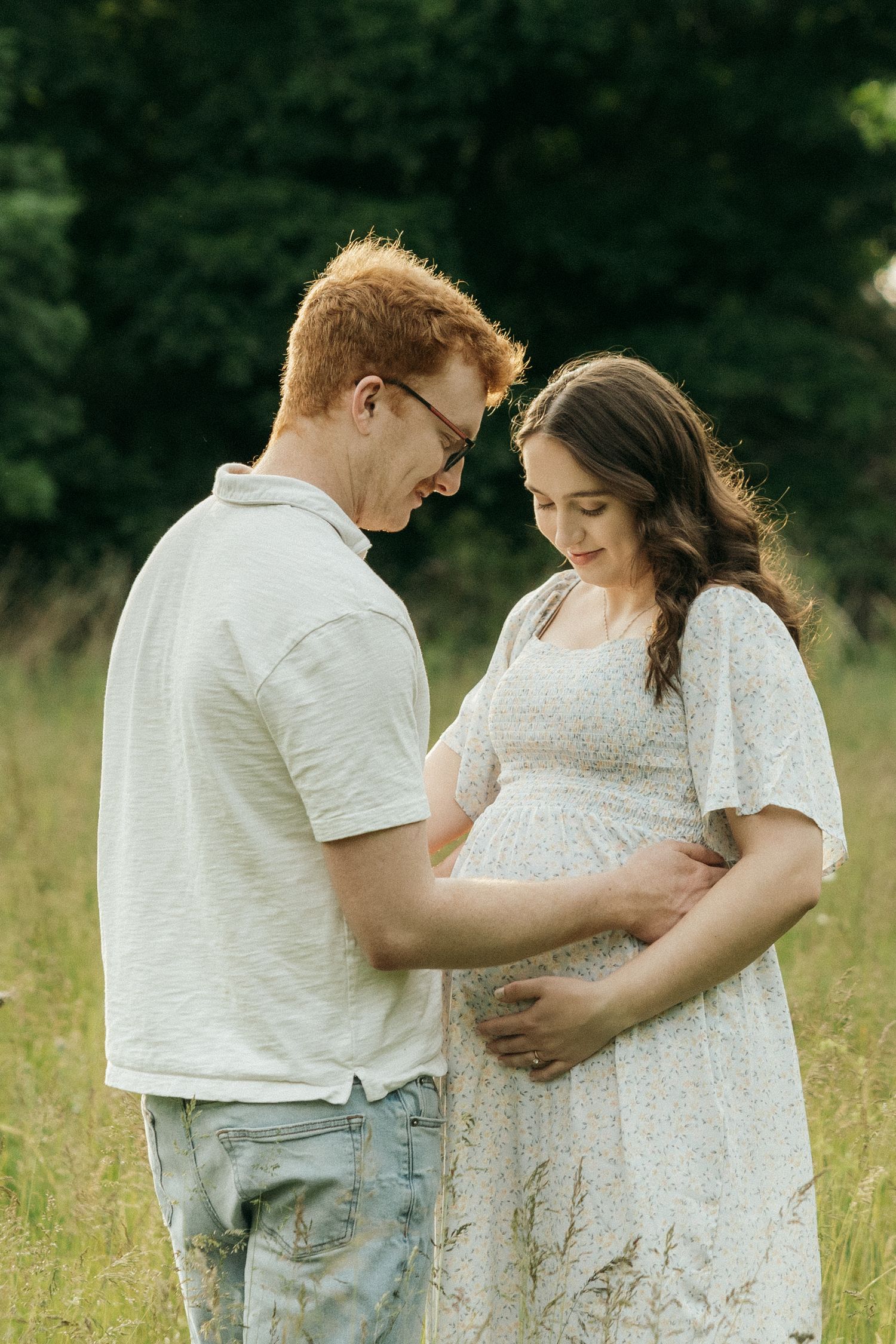 A couple sharing an intimate moment in a sunny meadow wearing white clothing.