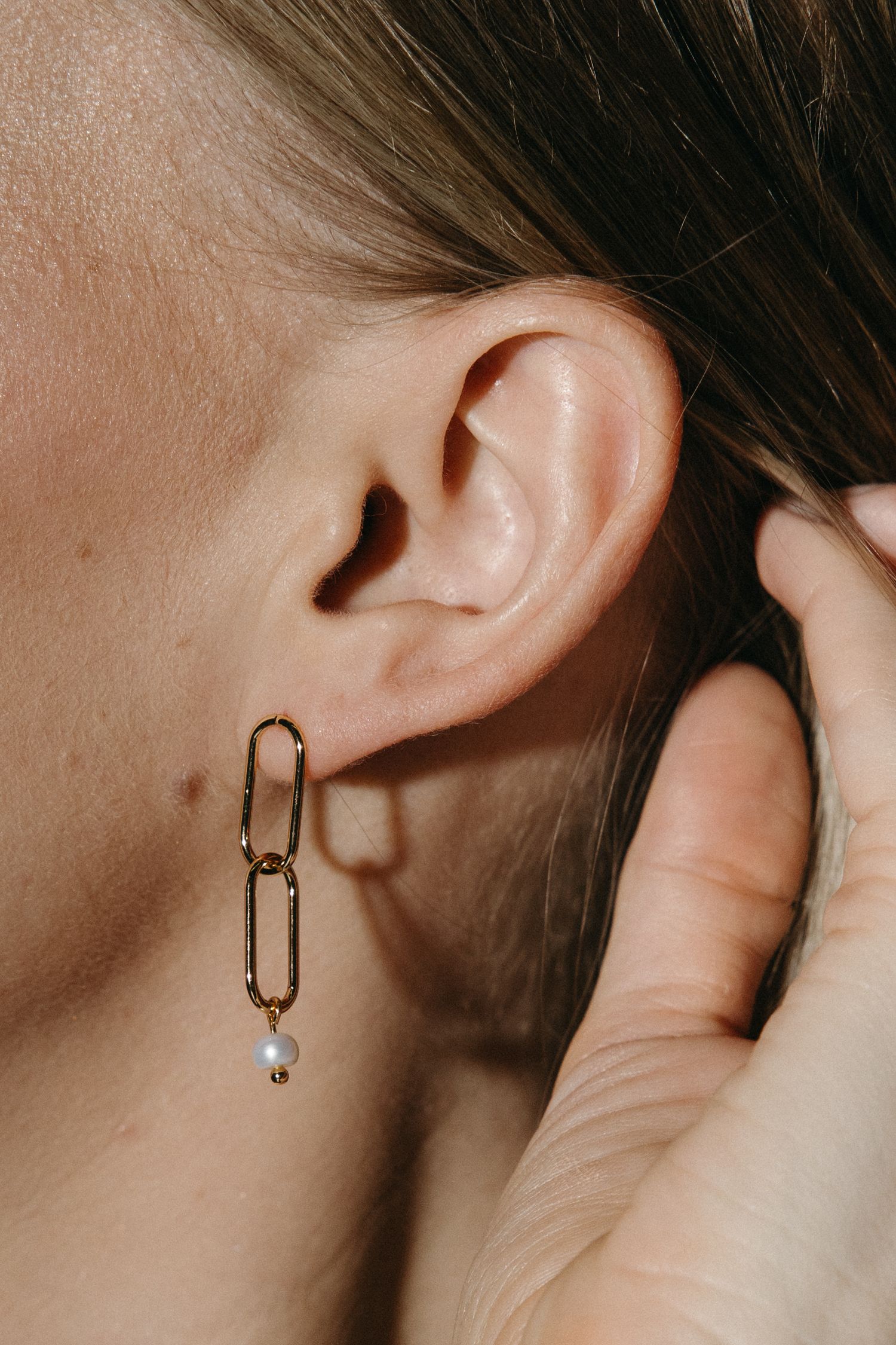 Close-up of an ear wearing a minimalist chain-link earring with a small pearl drop pendant.