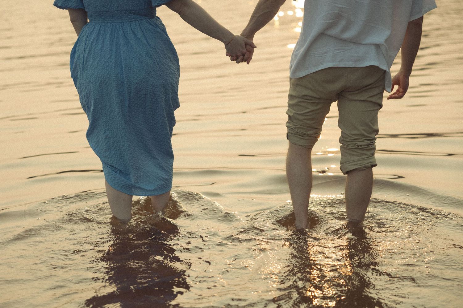 Couple's feet stand together in shallow ocean water during sunset.