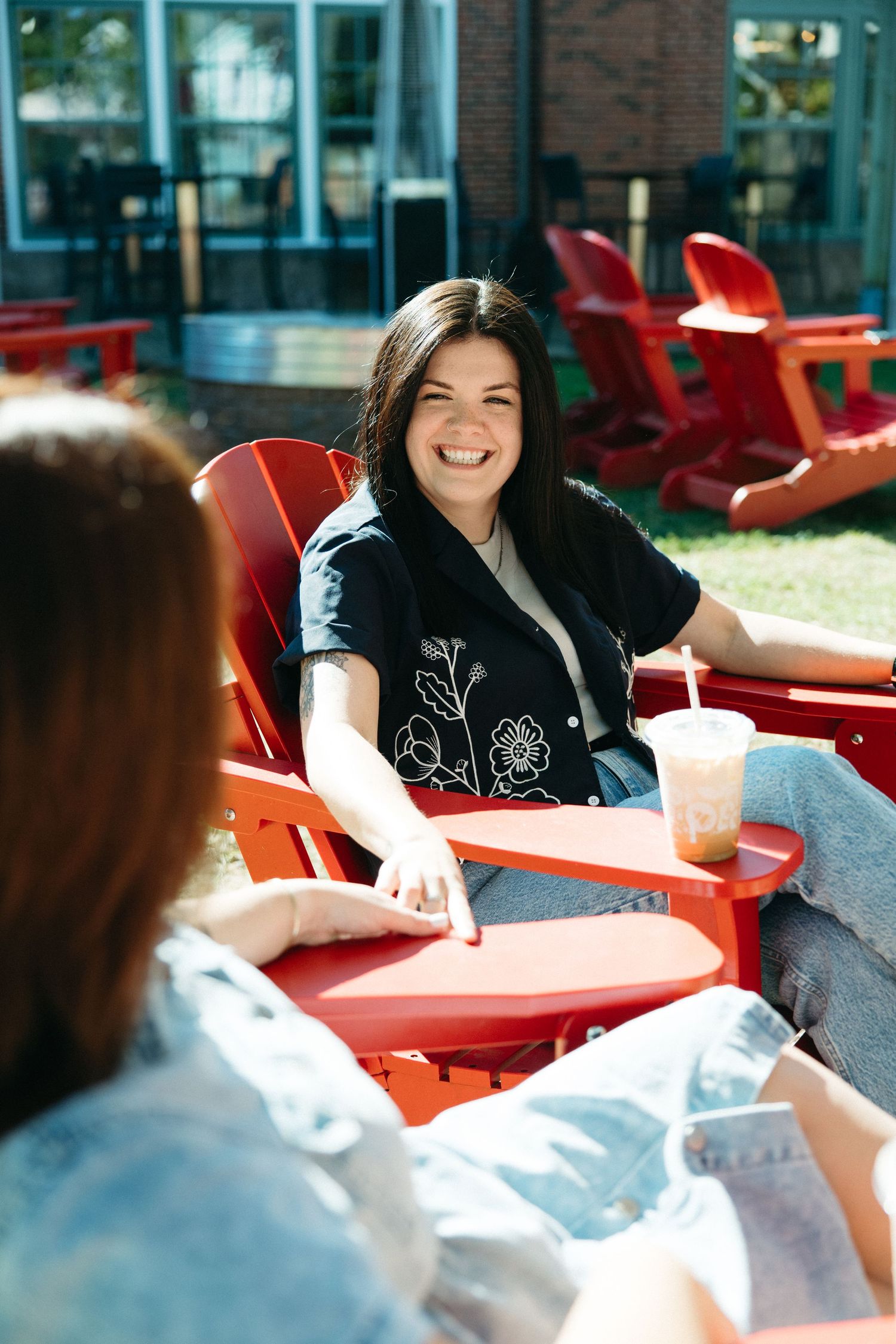People chatting and laughing while seated at red outdoor tables.