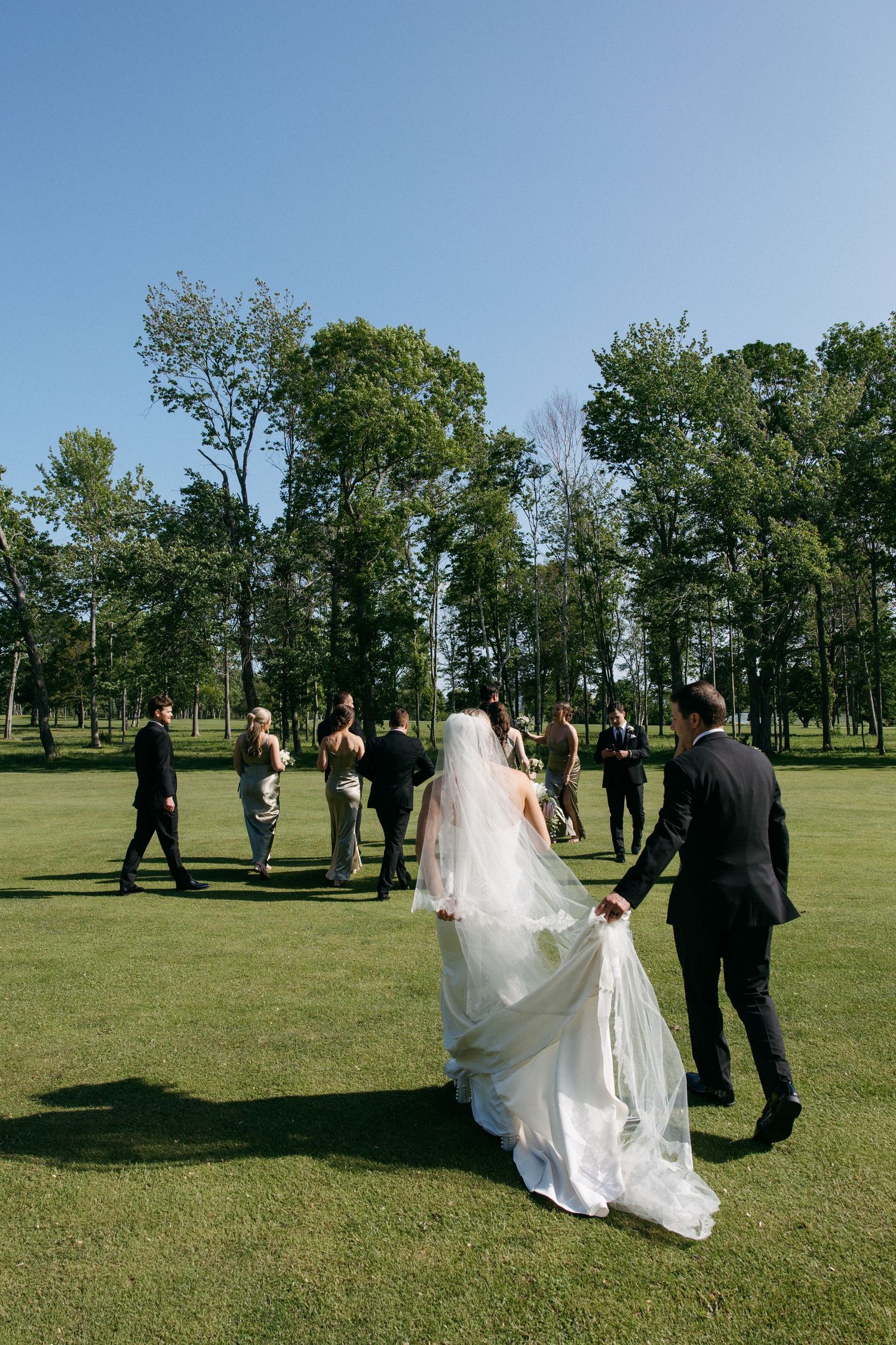 Wedding party walking across a green lawn during an outdoor photo session.