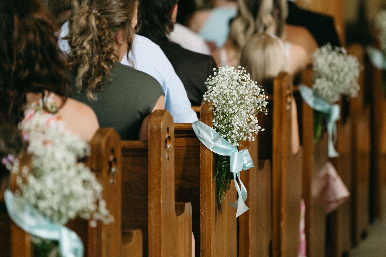 Church pews decorated with light blue ribbons and baby's breath flowers.