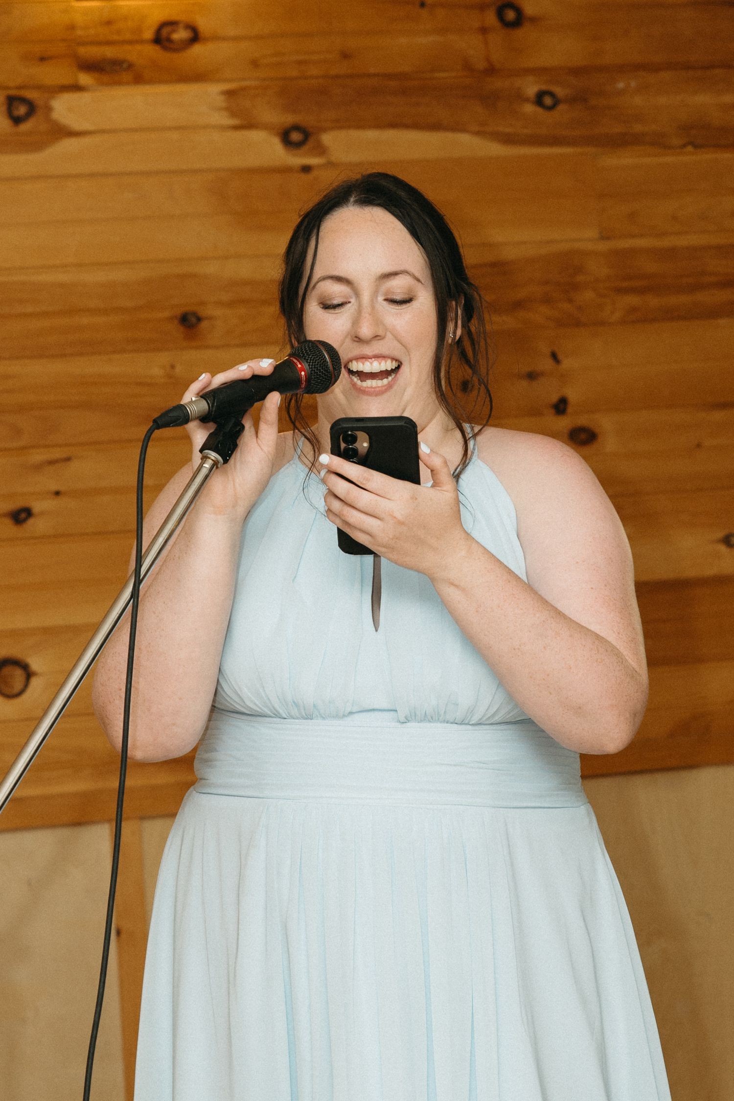 Person in light blue dress looking at phone while standing at microphone.