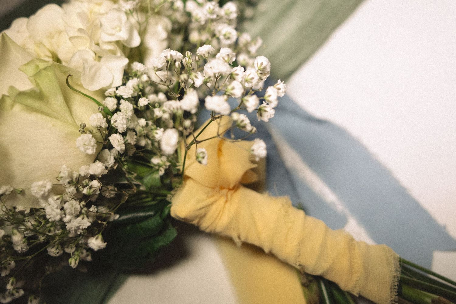 A wedding bouquet with white roses and baby's breath wrapped in cream-colored fabric.